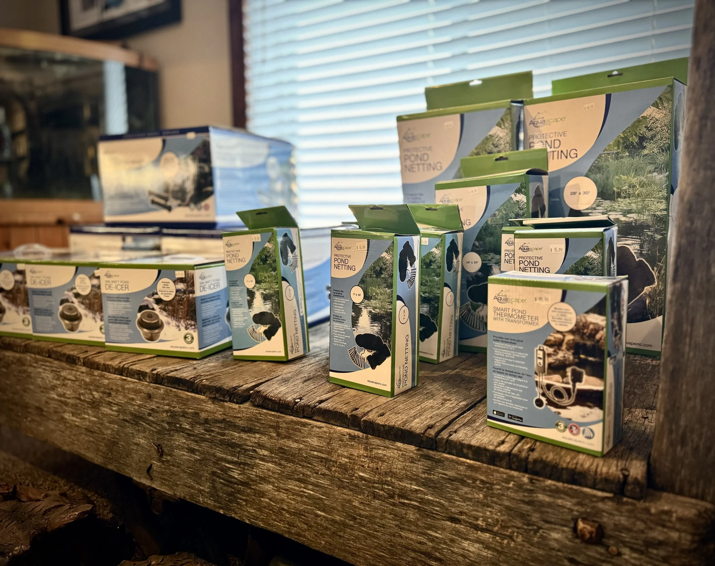 Multiple boxes of pond netting placed on a rustic wooden table, with a window with blinds in the background.