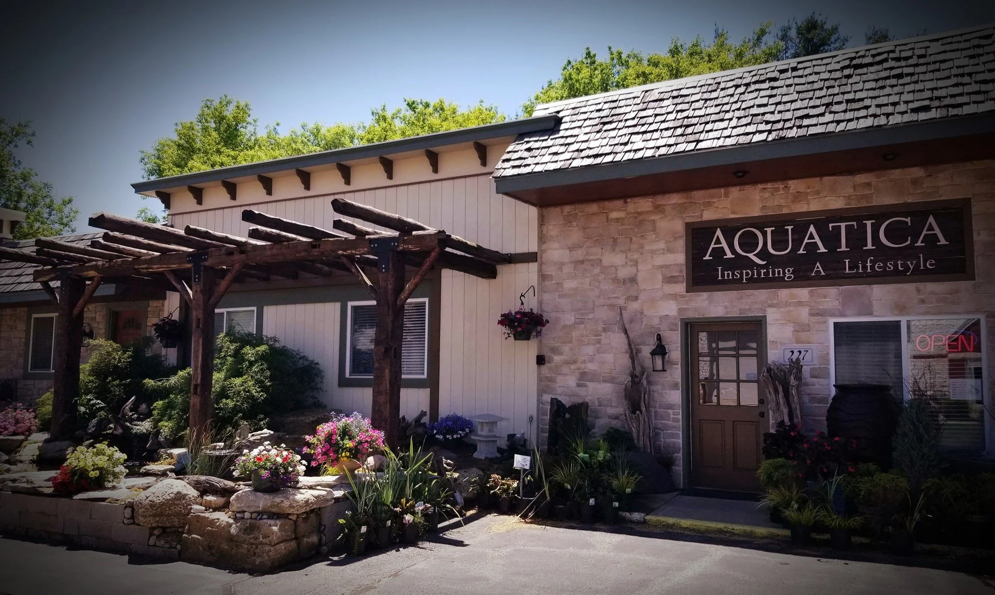 Exterior view of a building with a sign that reads 'AQUATICA Inspiring A Lifestyle,' surrounded by a garden with colorful flowers and trees in the background.