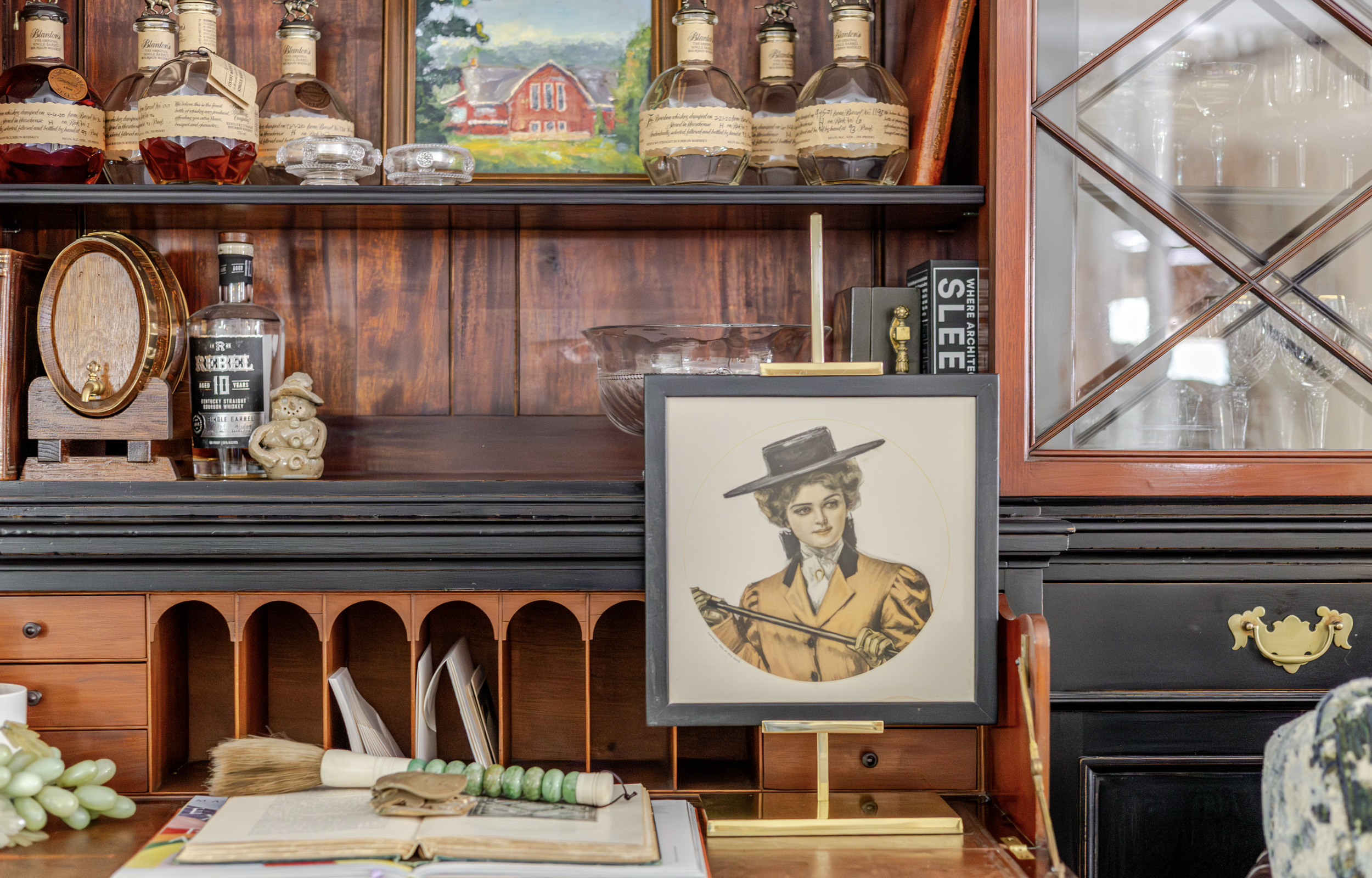 A vintage bar setup with bottles of liquor, a small keg, and a framed portrait of a woman in a yellow coat and hat. A painting and open notebook add a cozy, nostalgic feel.