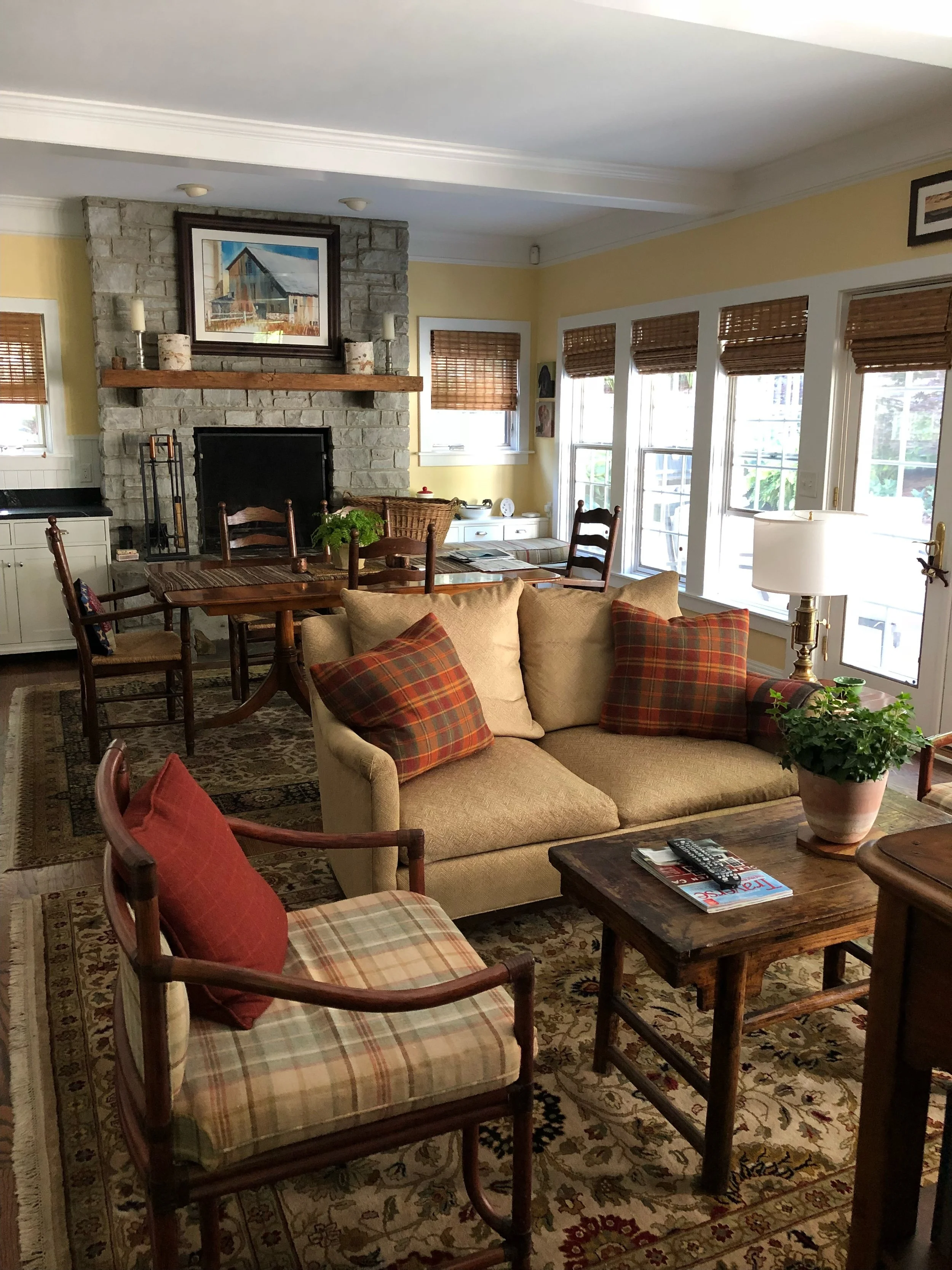 Warm living room with a stone fireplace, neutral sofa, plaid accent chairs, wooden furniture, and soft natural light.