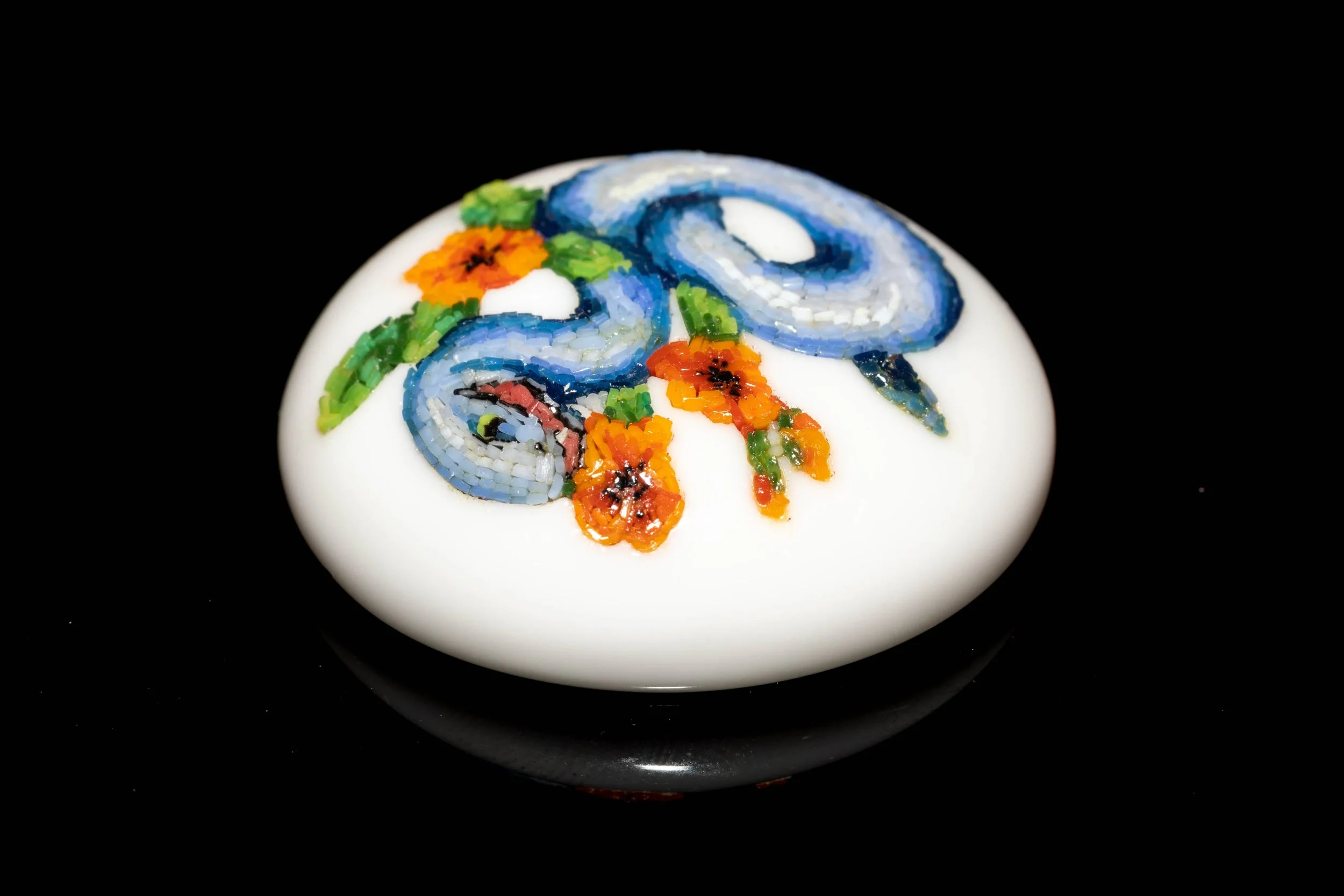 Low angled view of the blue snake micromosaic, showing the curved white glass cabochon and inset tesserae.