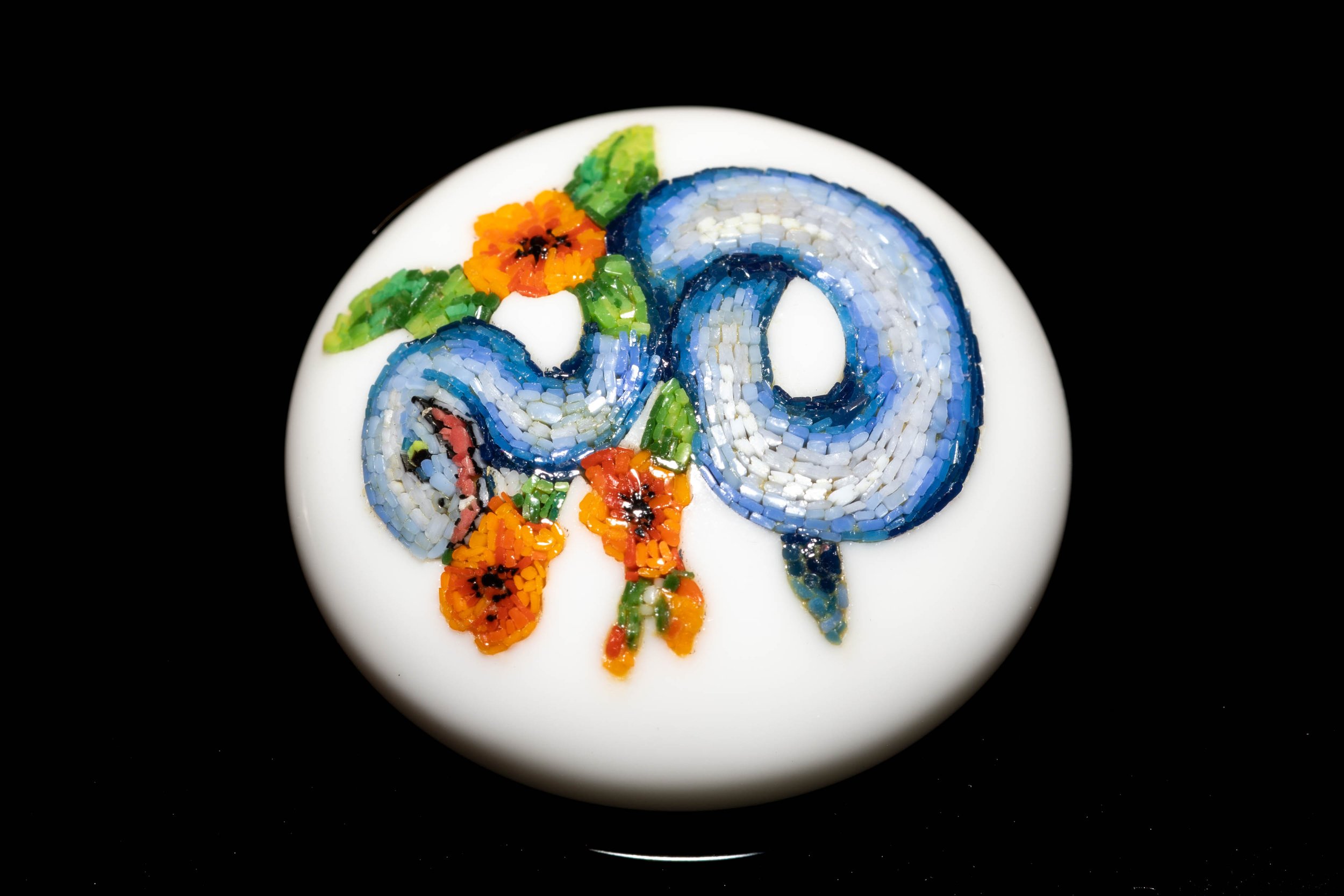 Angled view of the coiled blue snake and flowers in a carved white glass cabochon.