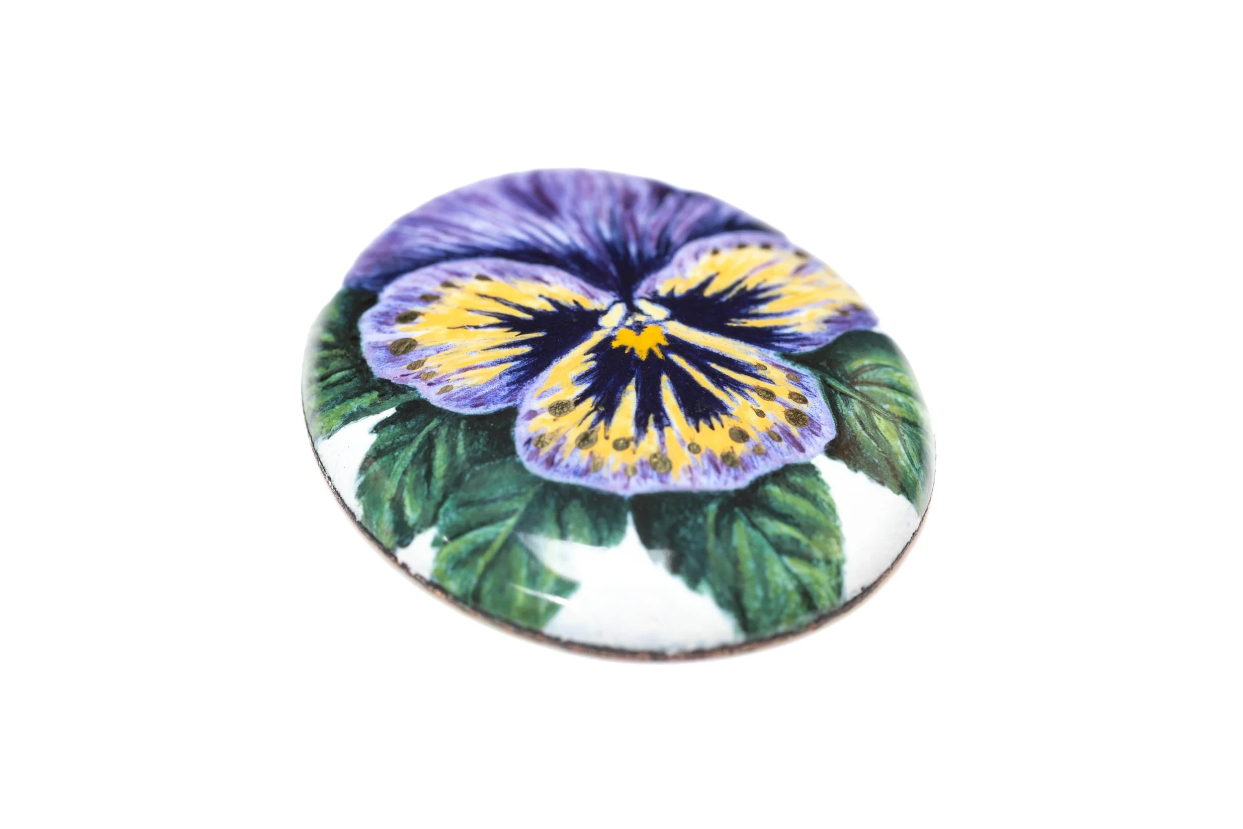 Angled view of the pansy enamel cabochon, showing the painted petals, green leaves and reflective surface.