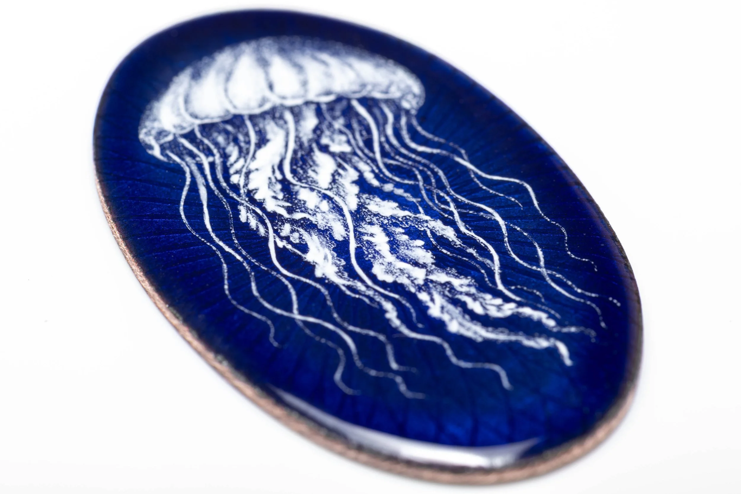 Close angled view of the white jellyfish and fine tentacles on the blue grisaille enamel cabochon.