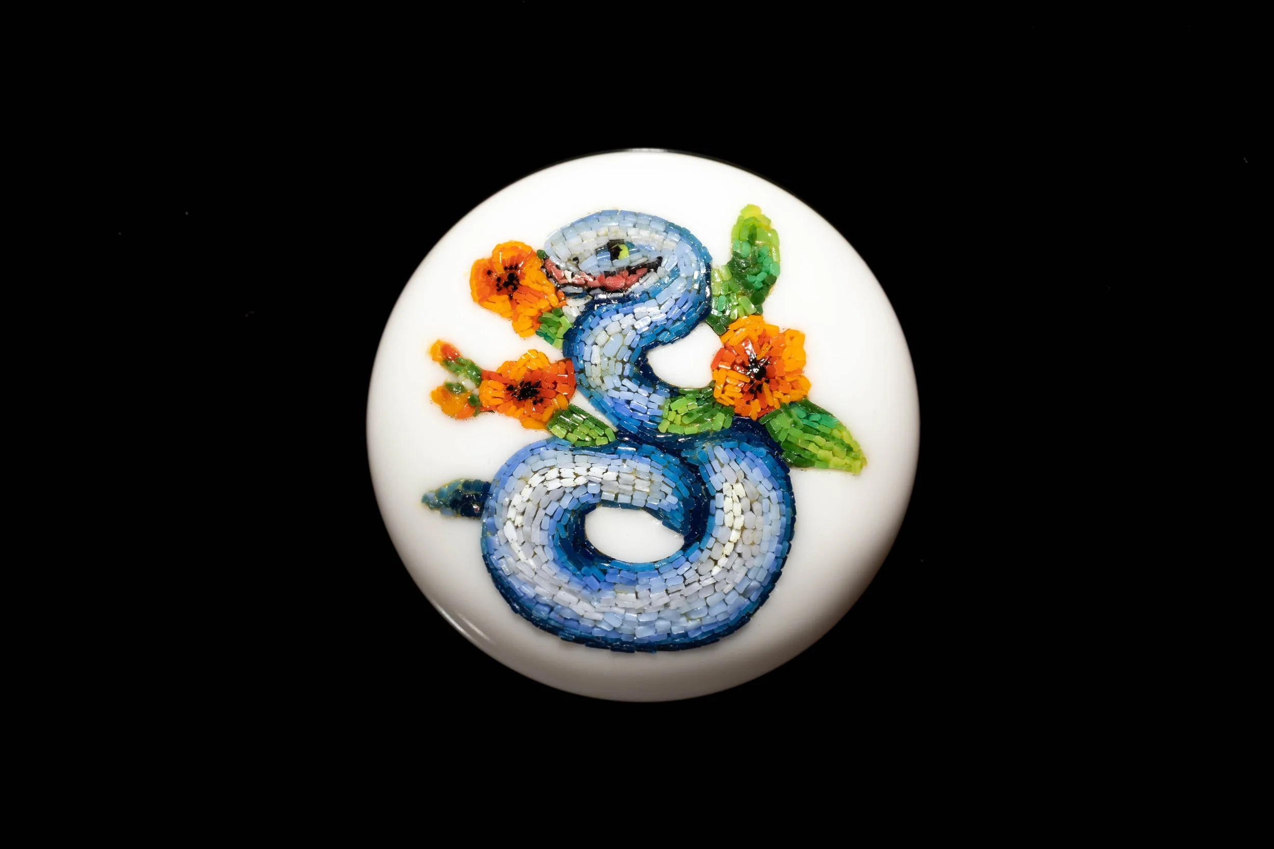 Coiled blue snake among orange flowers and green leaves, in micromosaic set into a round white glass cabochon.