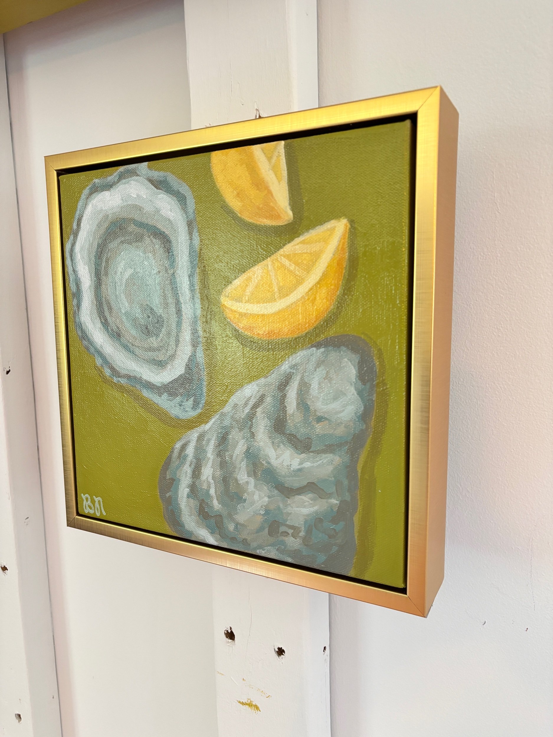 Oyster shell and lemon wedge painting on a rich green background in a gold frame, featuring coastal-inspired acrylic artwork with elegant Southern entertaining style.