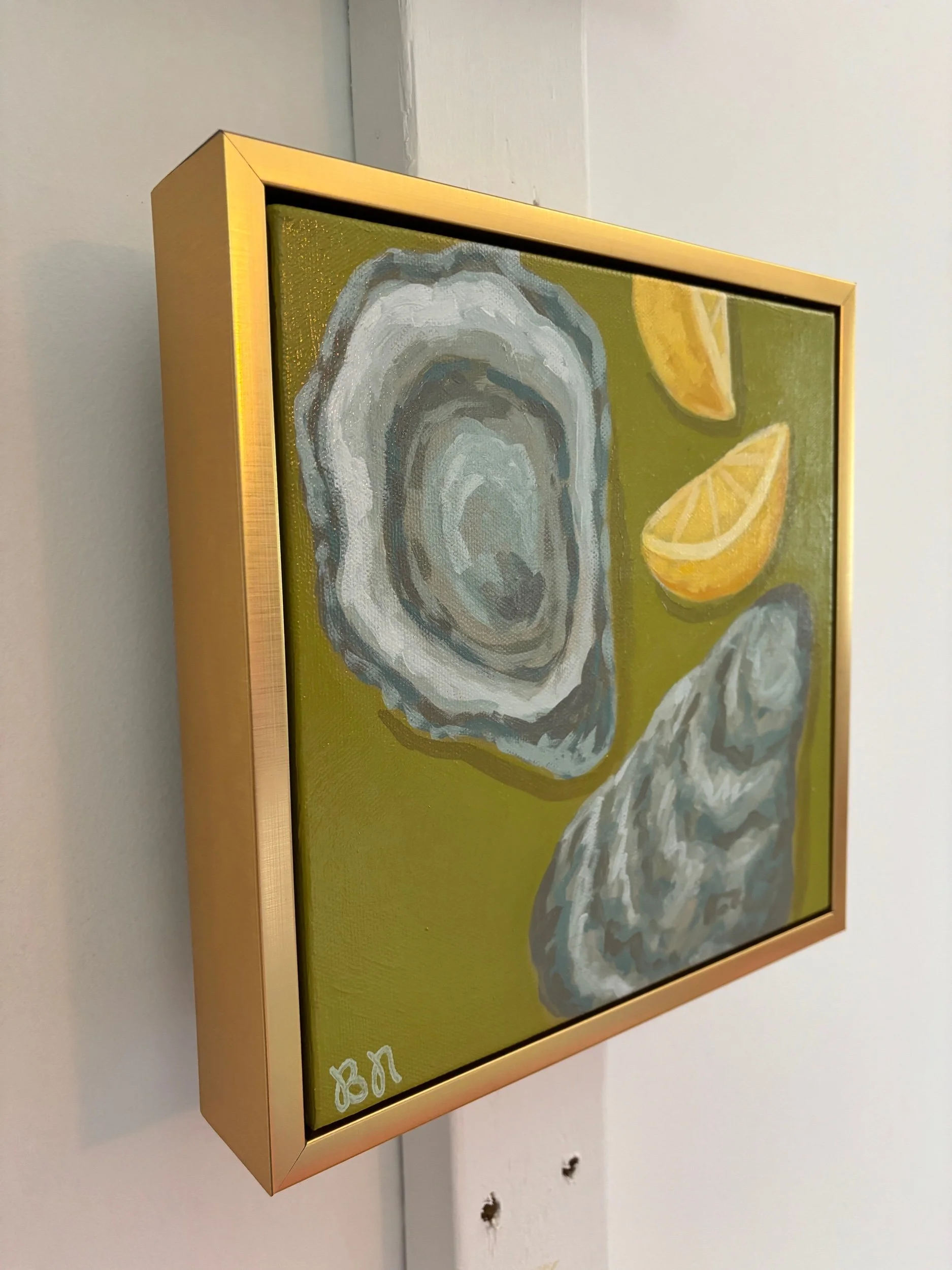 Oyster shell and lemon wedge painting on a rich green background in a gold frame, featuring coastal-inspired acrylic artwork with elegant Southern entertaining style.
