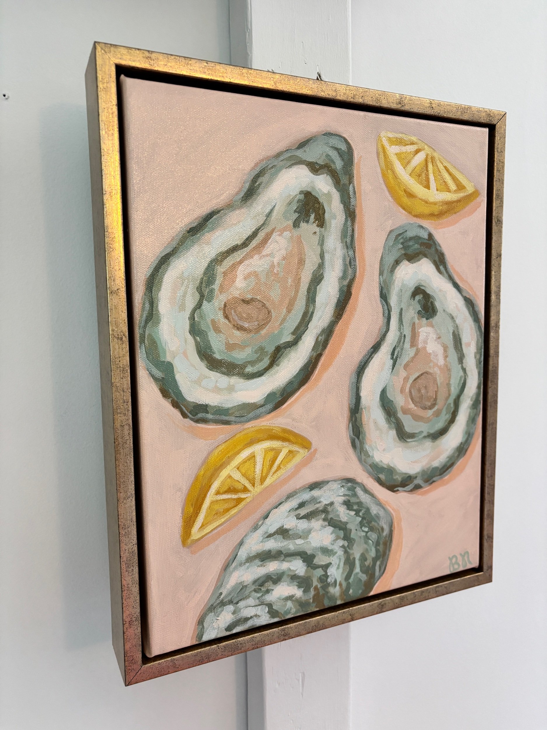 Original acrylic painting of an oyster shell and lemon wedge on a soft pink background in a gold frame, featuring elegant coastal-inspired artwork with Southern entertaining charm.