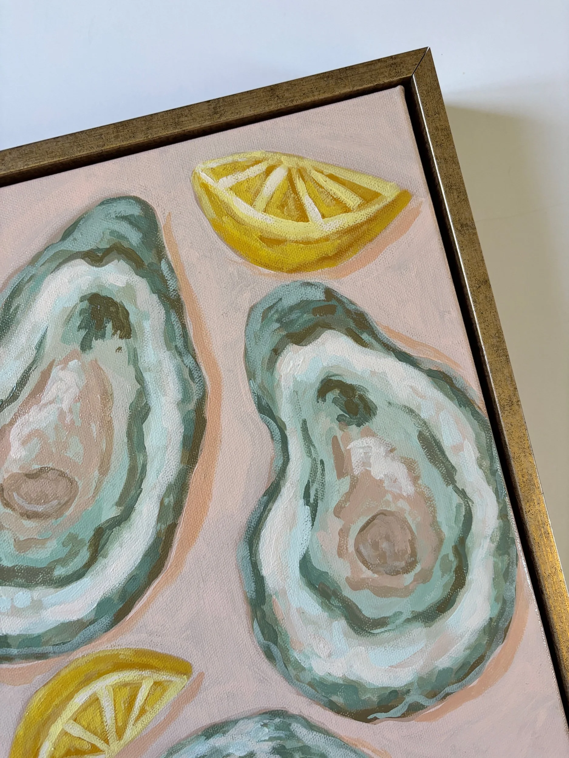 Original acrylic painting of an oyster shell and lemon wedge on a soft pink background in a gold frame, featuring elegant coastal-inspired artwork with Southern entertaining charm.