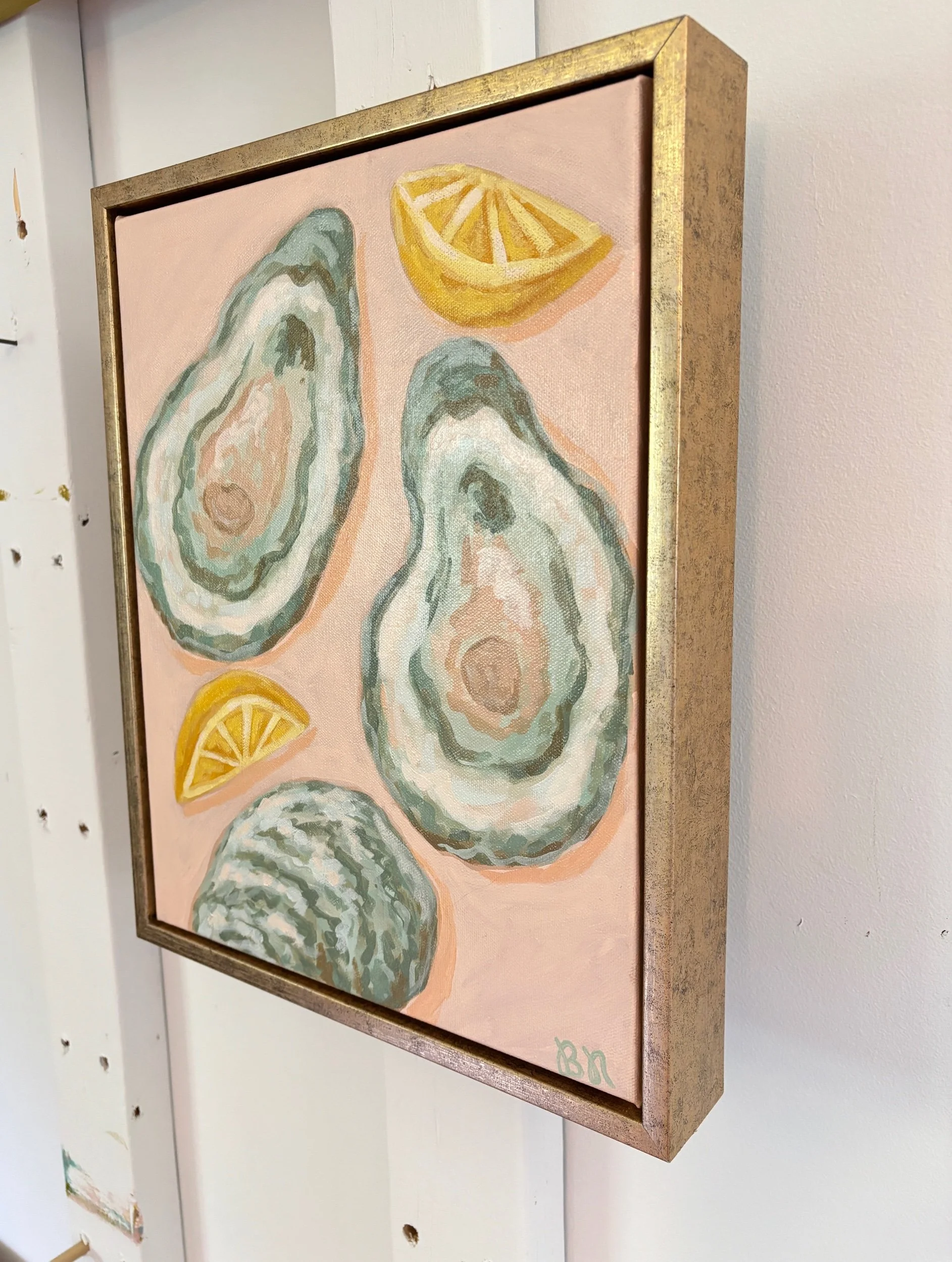 Original acrylic painting of an oyster shell and lemon wedge on a soft pink background in a gold frame, featuring elegant coastal-inspired artwork with Southern entertaining charm.