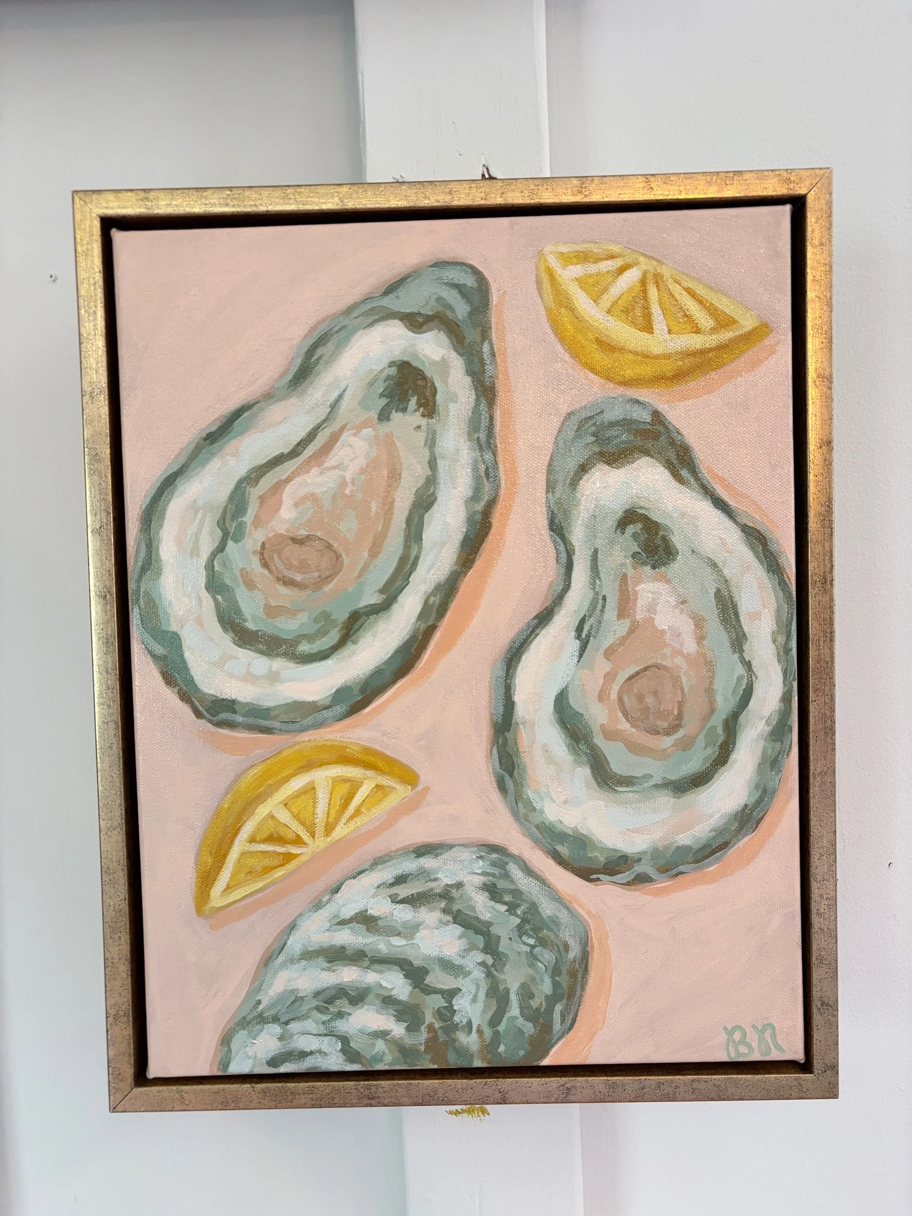 Original acrylic painting of an oyster shell and lemon wedge on a soft pink background in a gold frame, featuring elegant coastal-inspired artwork with Southern entertaining charm.