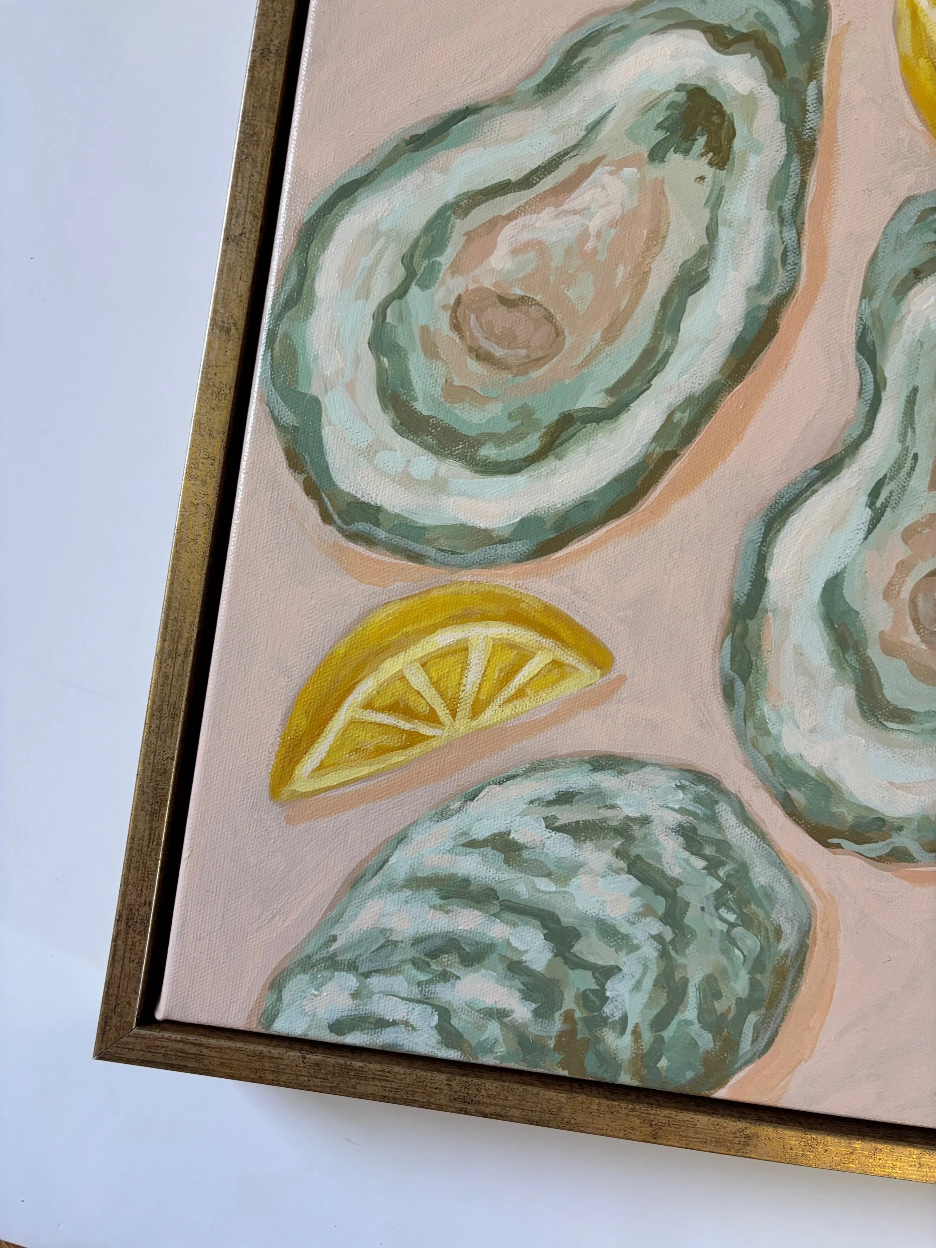 Original acrylic painting of an oyster shell and lemon wedge on a soft pink background in a gold frame, featuring elegant coastal-inspired artwork with Southern entertaining charm.