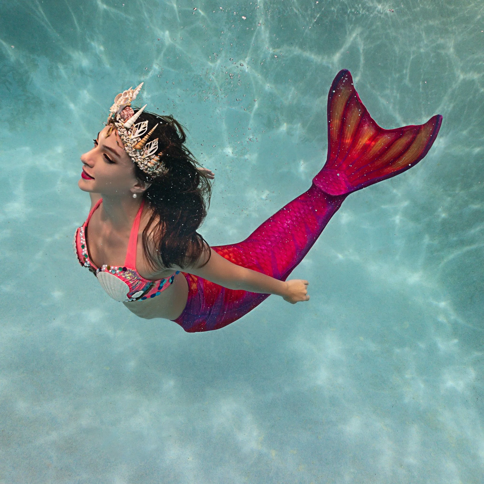 Roxy in a bright pink mermaid tail with a shell crown performing in a heated pool in Orlando, FL