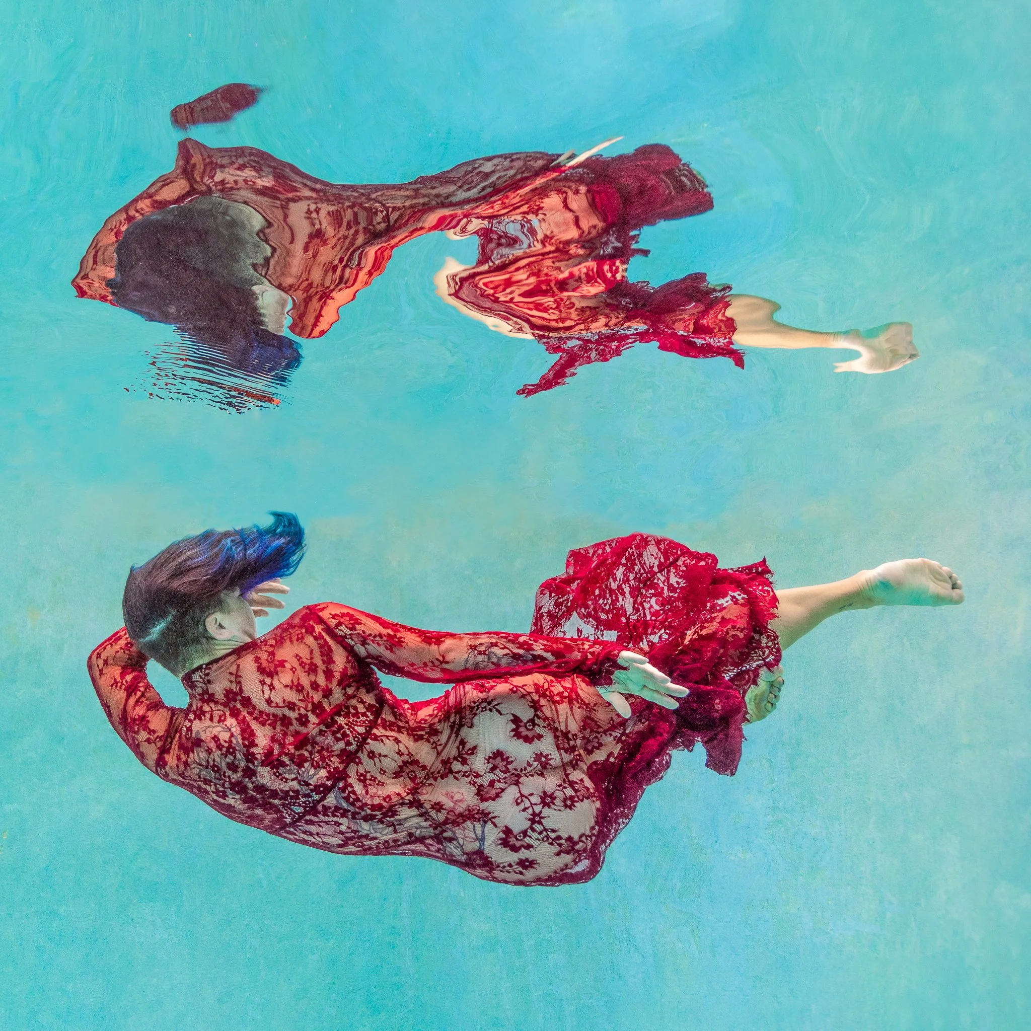 Mechelina floats just under the surface in a red lace dress, with her reflection above, in a heated pool in Orlando, FL
