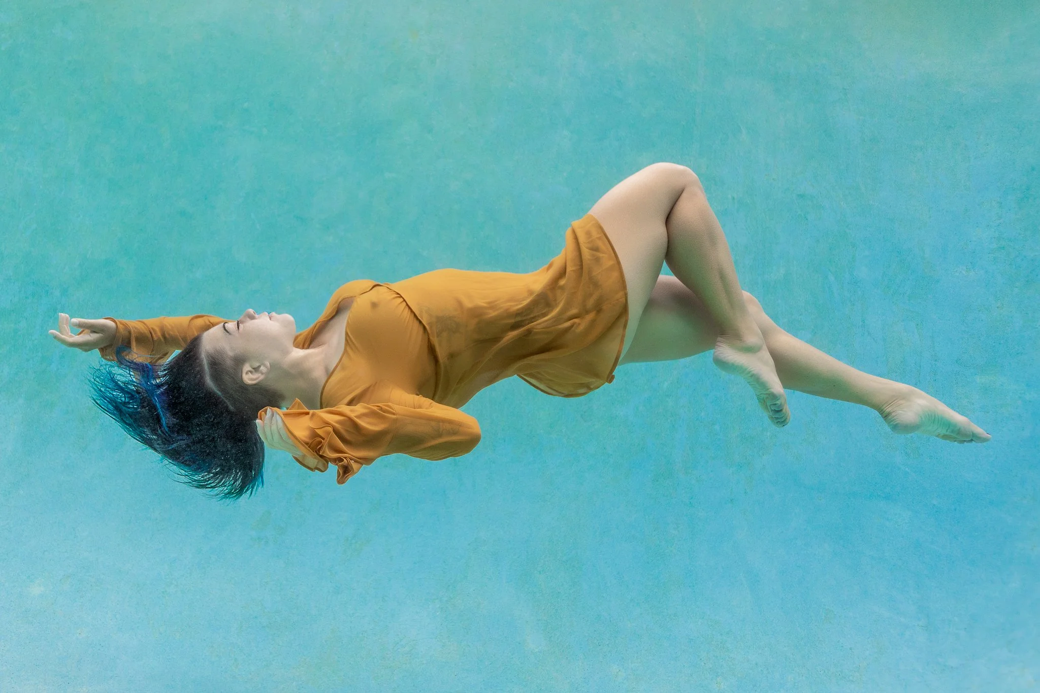 Michelina floats horizontally in a flowing gold dress, underwater in a heated pool in Orlando, FL