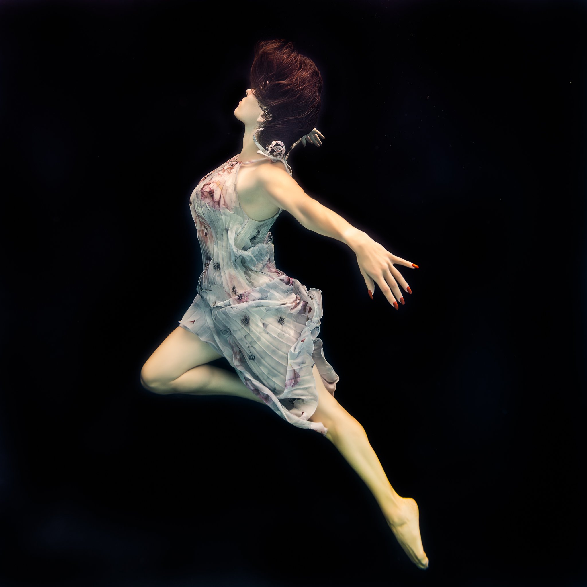 Cristina in a flower dress poses on a black background underwater in a heated pool in Orlando, FL