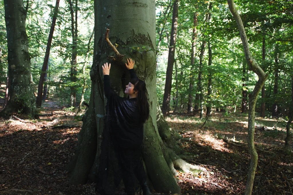 Eine junge Frau umarmt einen großen Baum im Wald.