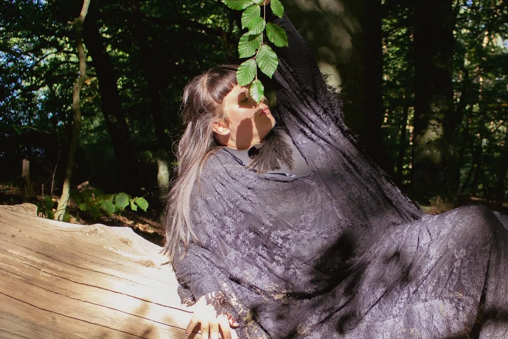 Eine Frau sitzt entspannt an einem Baum im Wald, die Augen geschlossen, mit Sonnenlicht, das durch die Blätter fällt.