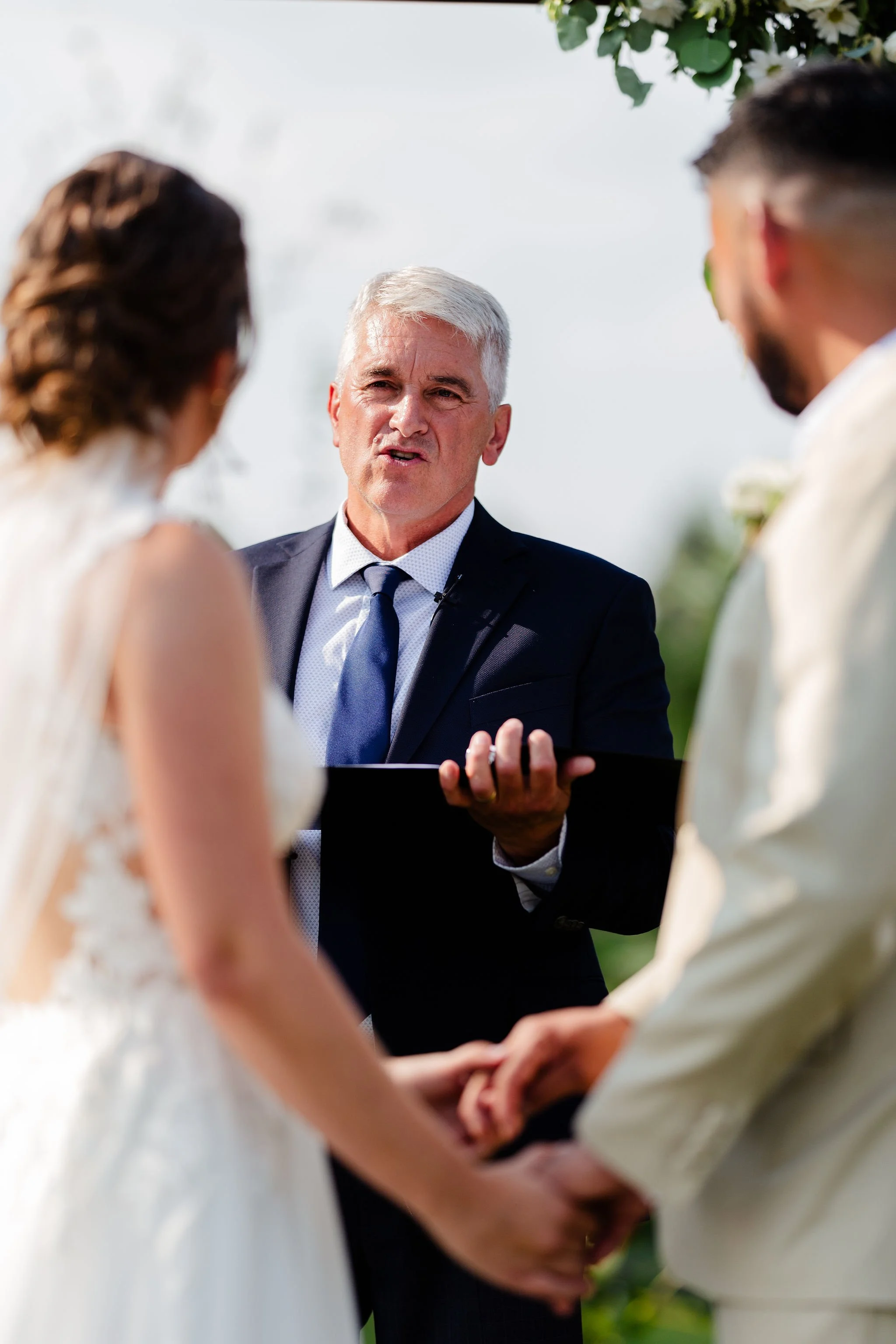 A couple getting married holding hands, with an officiant conducting the ceremony outdoors.