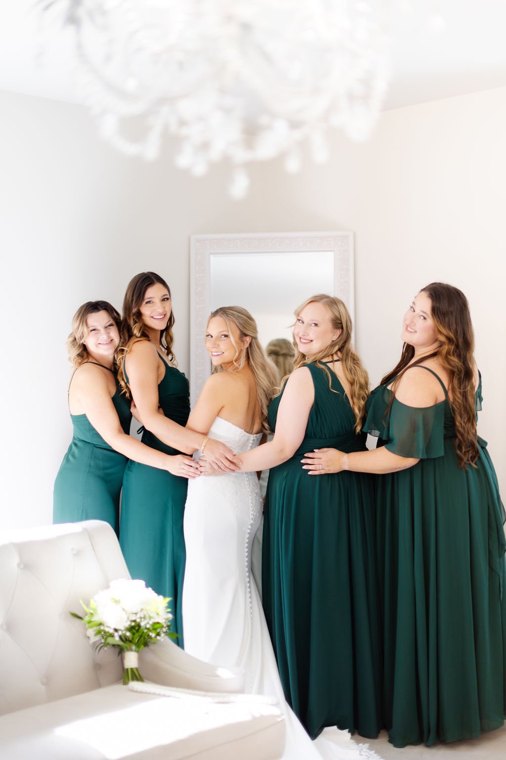 Bride and five bridesmaids in green dresses standing together in a bright room, smiling at the camera.