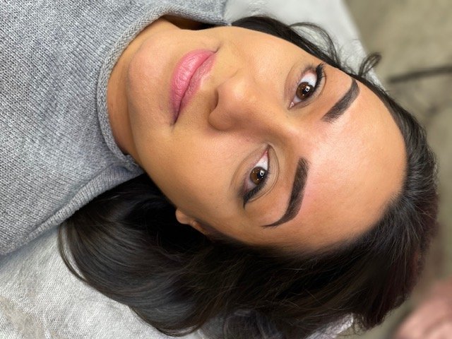 A woman with long dark hair and well-defined eyebrows lying down on her side, looking at the camera with a neutral expression.