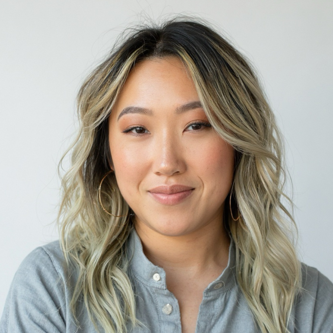 A woman with shoulder-length wavy blonde hair, wearing hoop earrings and a light gray button-up shirt, smiling softly at the camera.