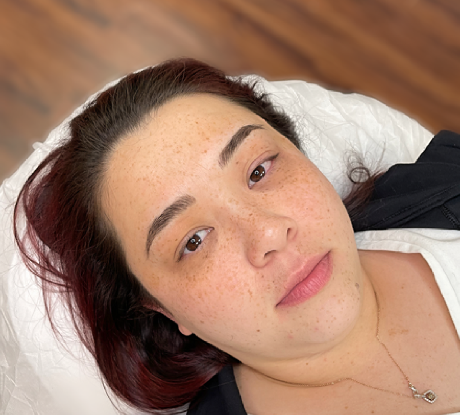 A woman with dark hair and freckles lying on a white pillow, looking at the camera.