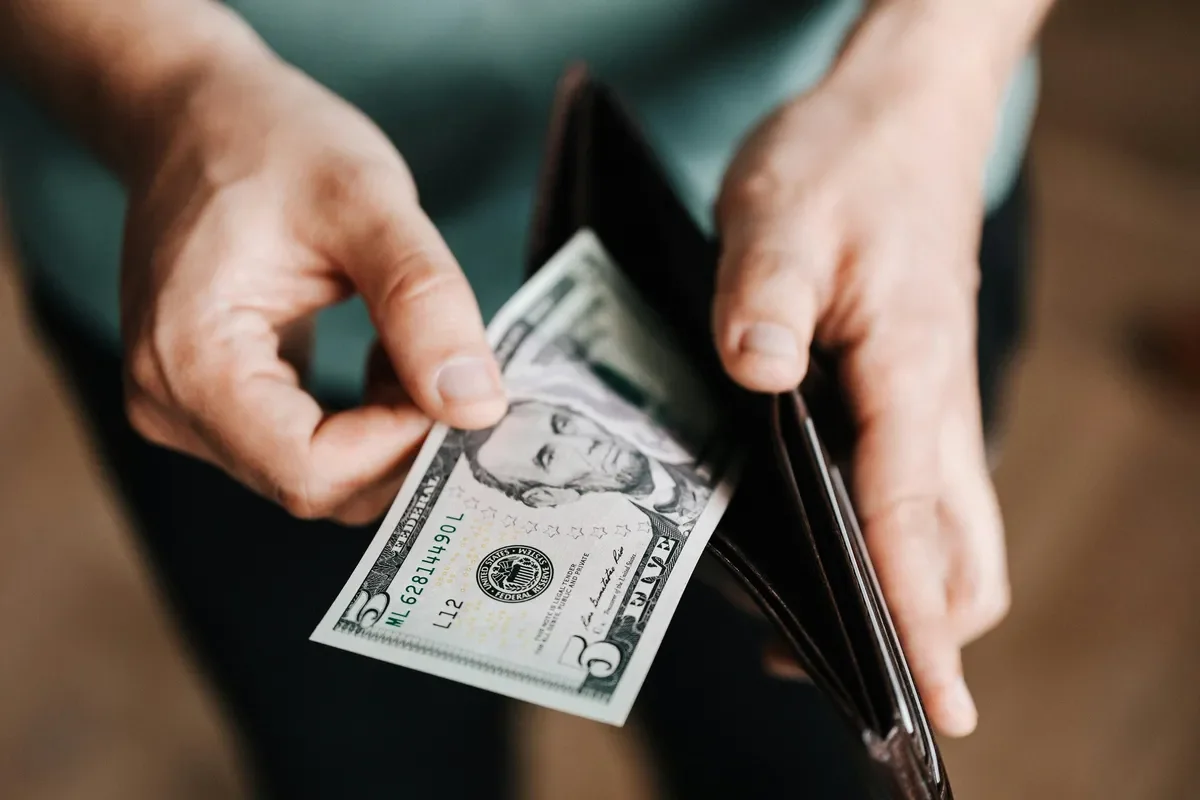 Close-up of hands holding a five-dollar bill and a wallet.