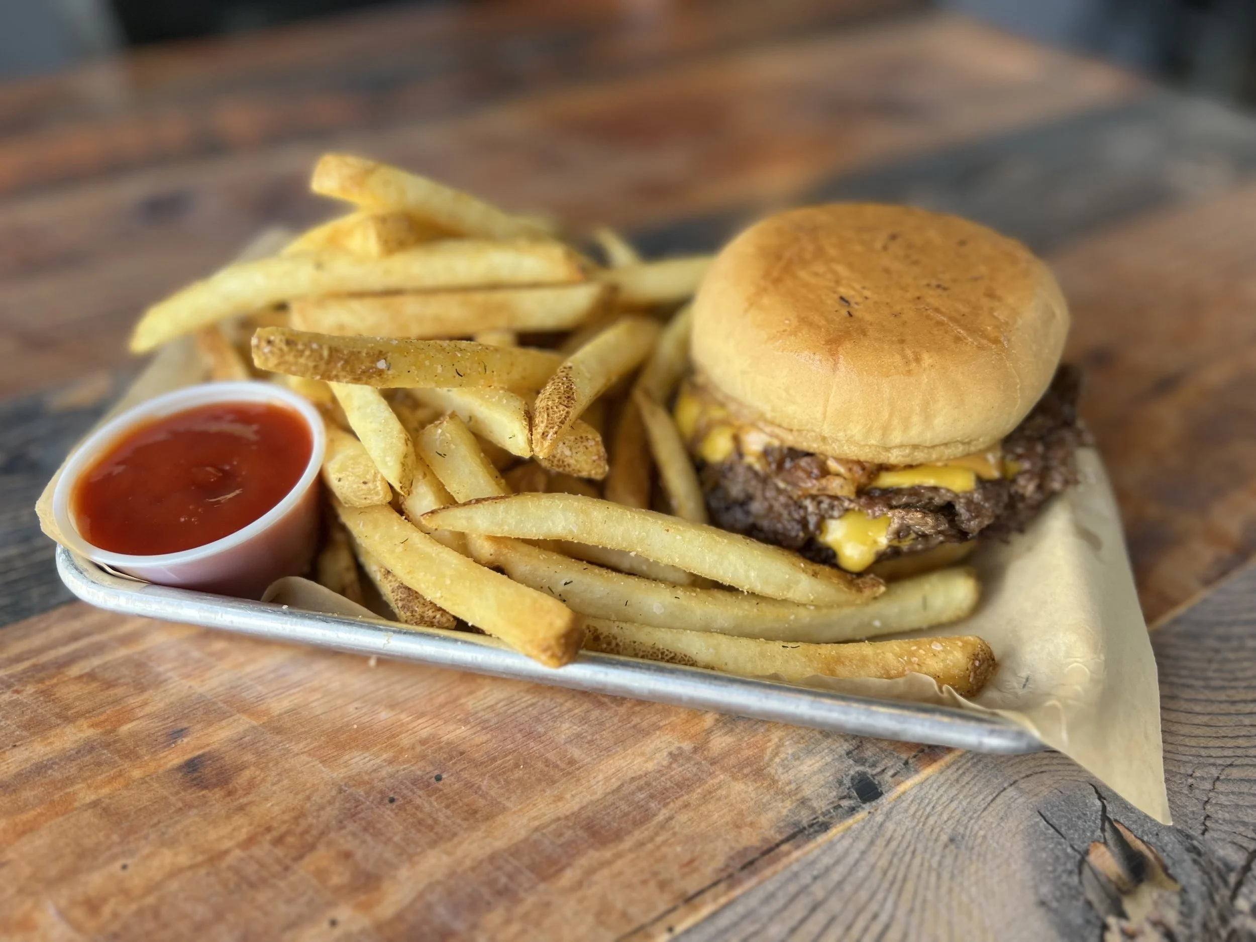 Closeup of a cheese burger, french fries and bowl of ketchup
