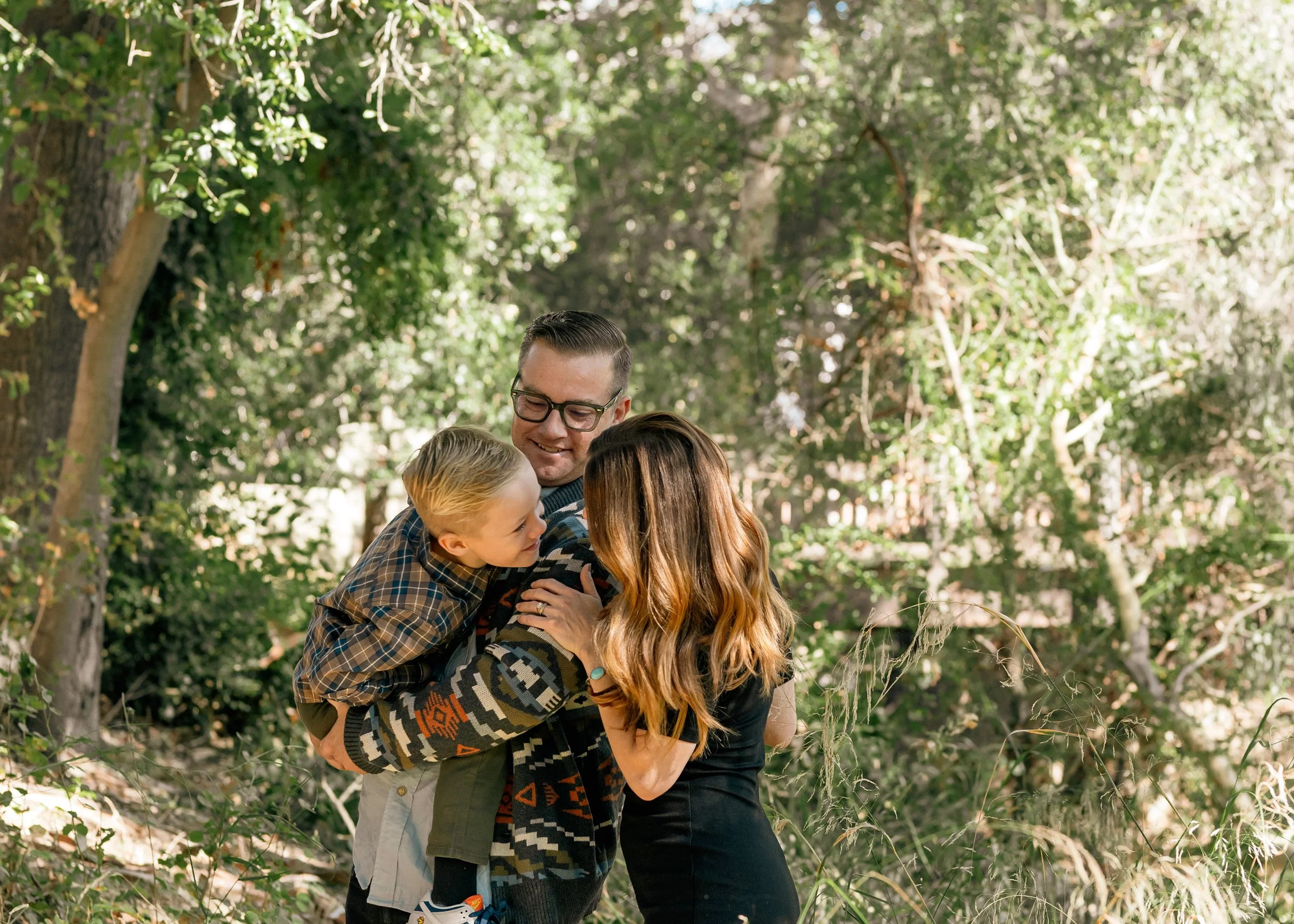 Family of three- lovingly giving their son attention, whilst dad holds his son, and mom interacts with him