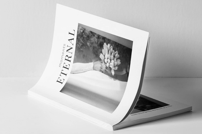 A magazine titled 'moments ETERNAL' with a black and white photo of a person holding a bouquet of flowers, placed on a white surface.