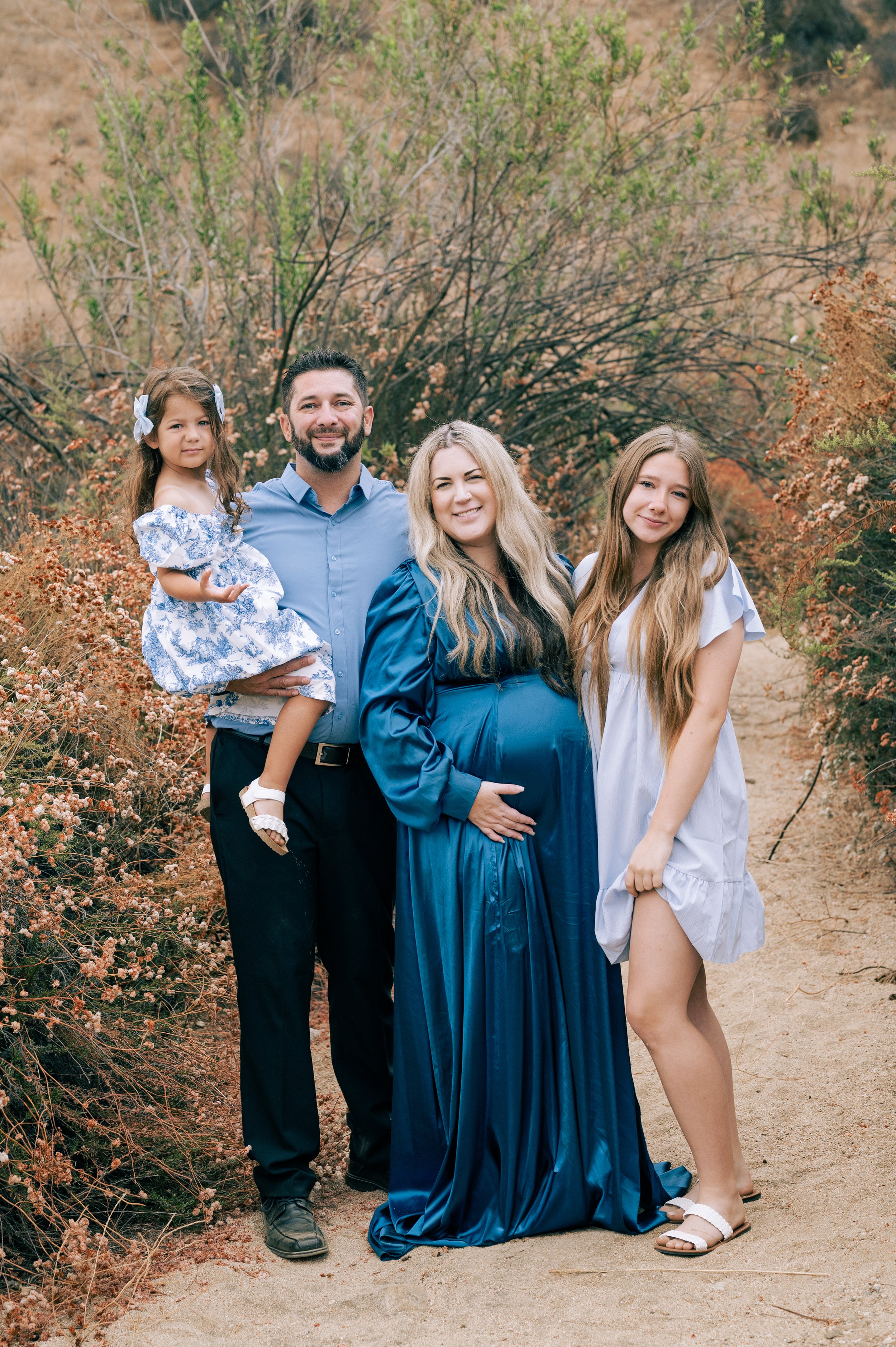 Pregnant mom with her two daughters and husband in front of fall foliage
