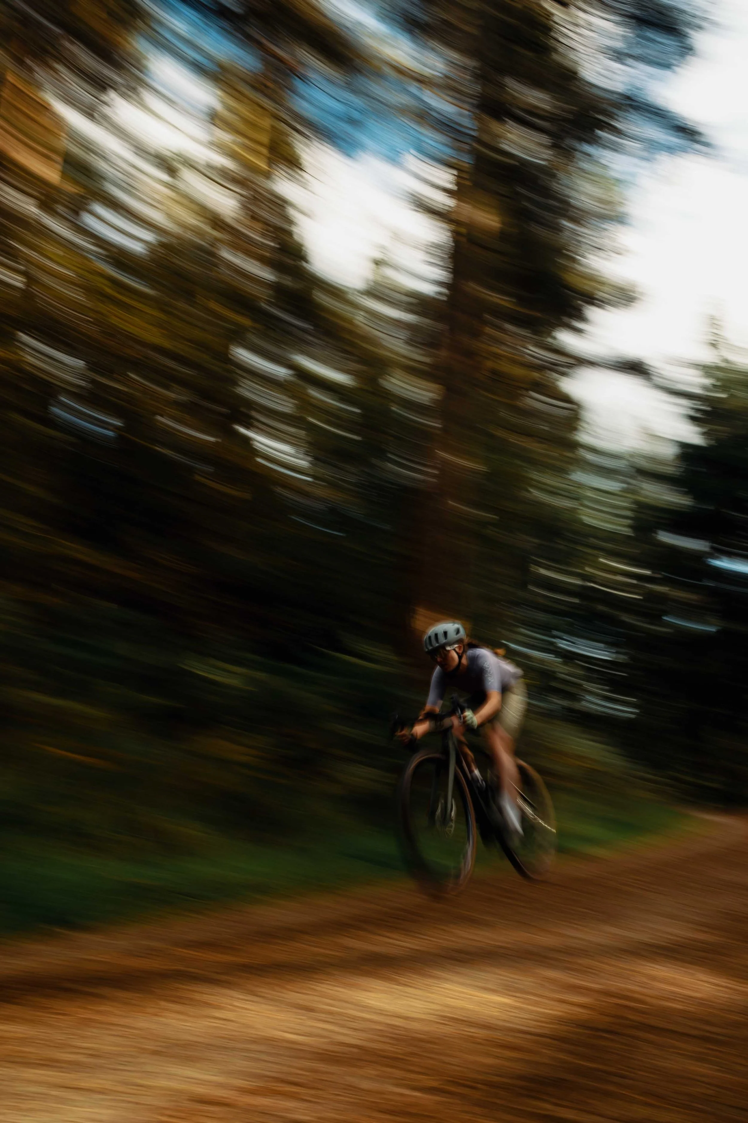 A person riding a mountain bike through a forest, with trees in the background appearing blurred due to motion.