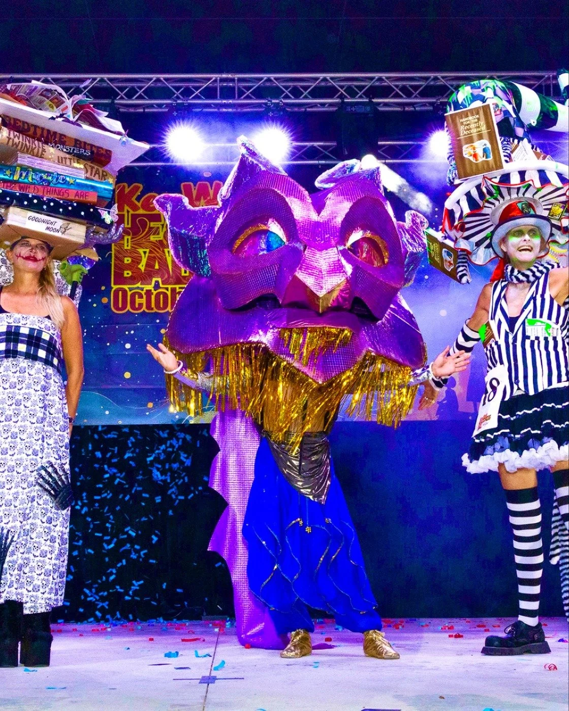 A person dressed in a colorful, elaborate costume with a large, intricate headpiece at a themed event or ball.