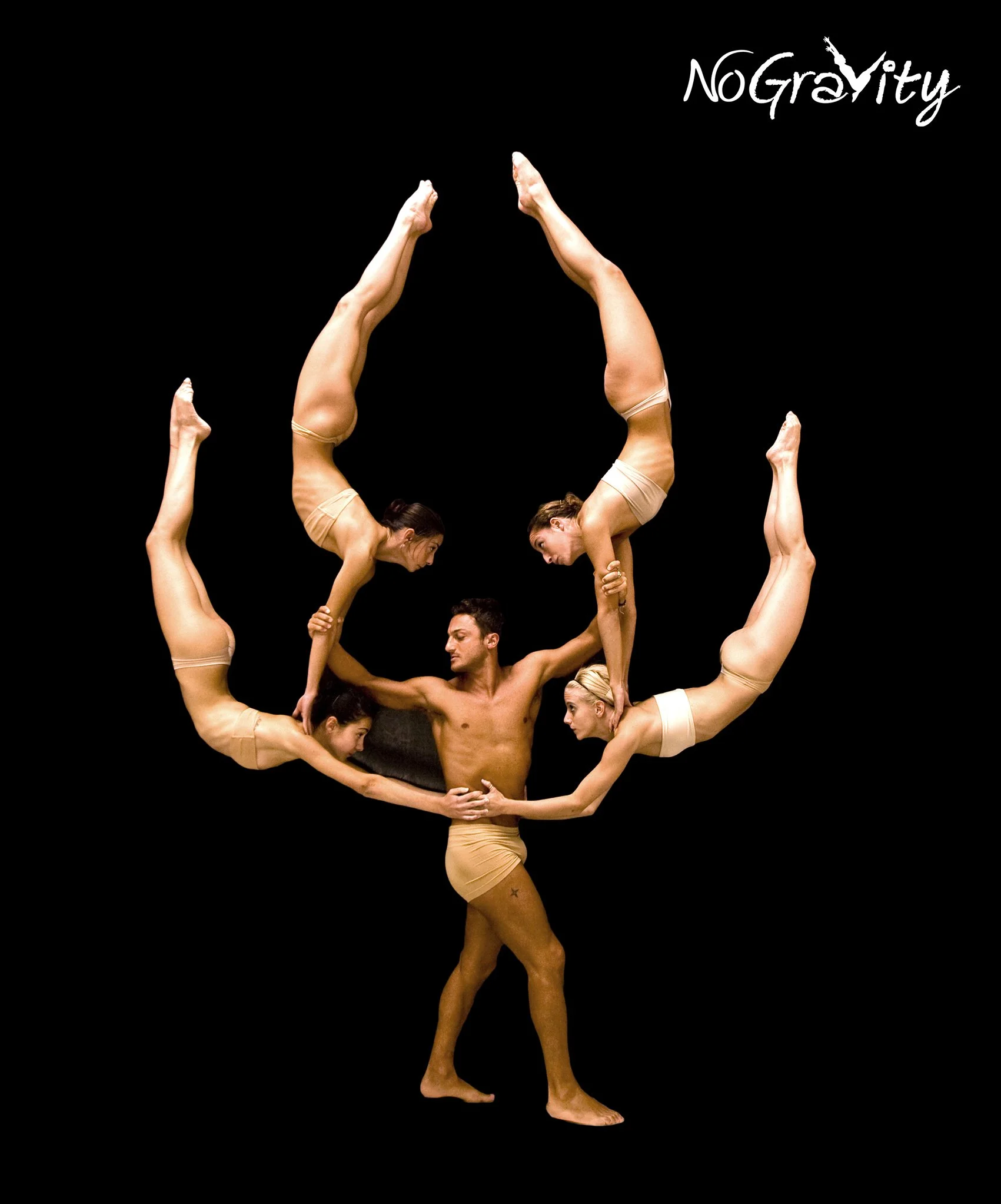 Group of six acrobats forming a balanced pose with their bodies and arms, with two women holding each other upside down with legs extended upward, and a man at the center supporting a woman in a handstand, all wearing beige costumes against a black background.