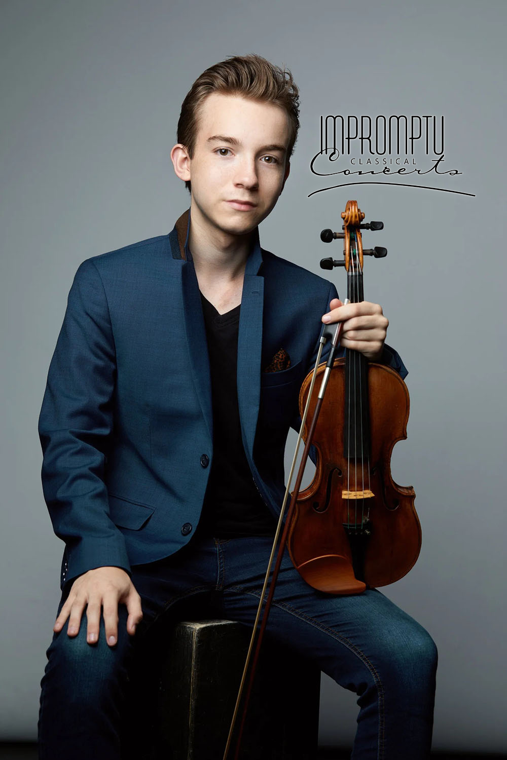 A young man in a blue blazer and black shirt holds a violin and a bow, sitting on a stool against a gray background. Text overlays the image, reading 'Impromptu Classical Concert'.