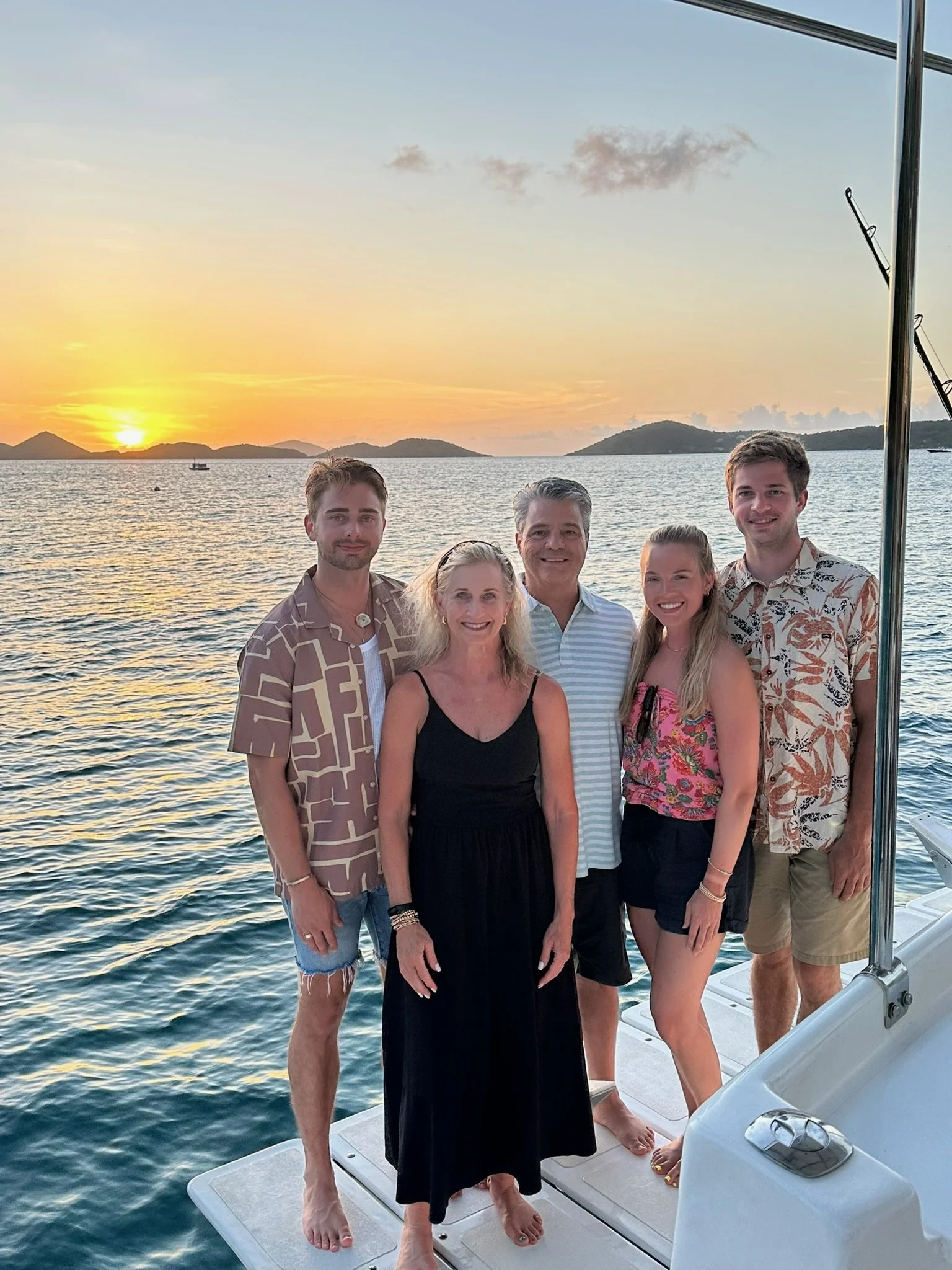 Happy Guests standing on RumAway at sunset with water and islands in the background.