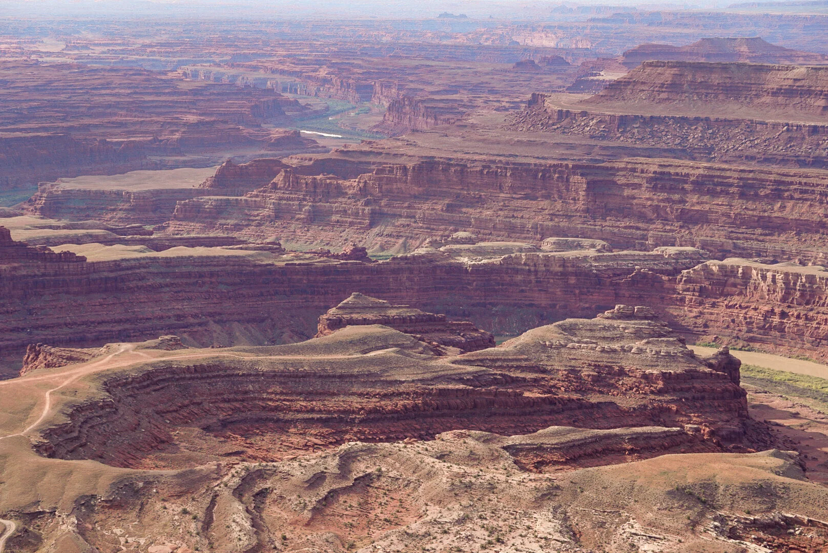 Aerial view of the Grand Canyon showing layered red and brown rock formations, steep cliffs, and a winding river at the bottom.