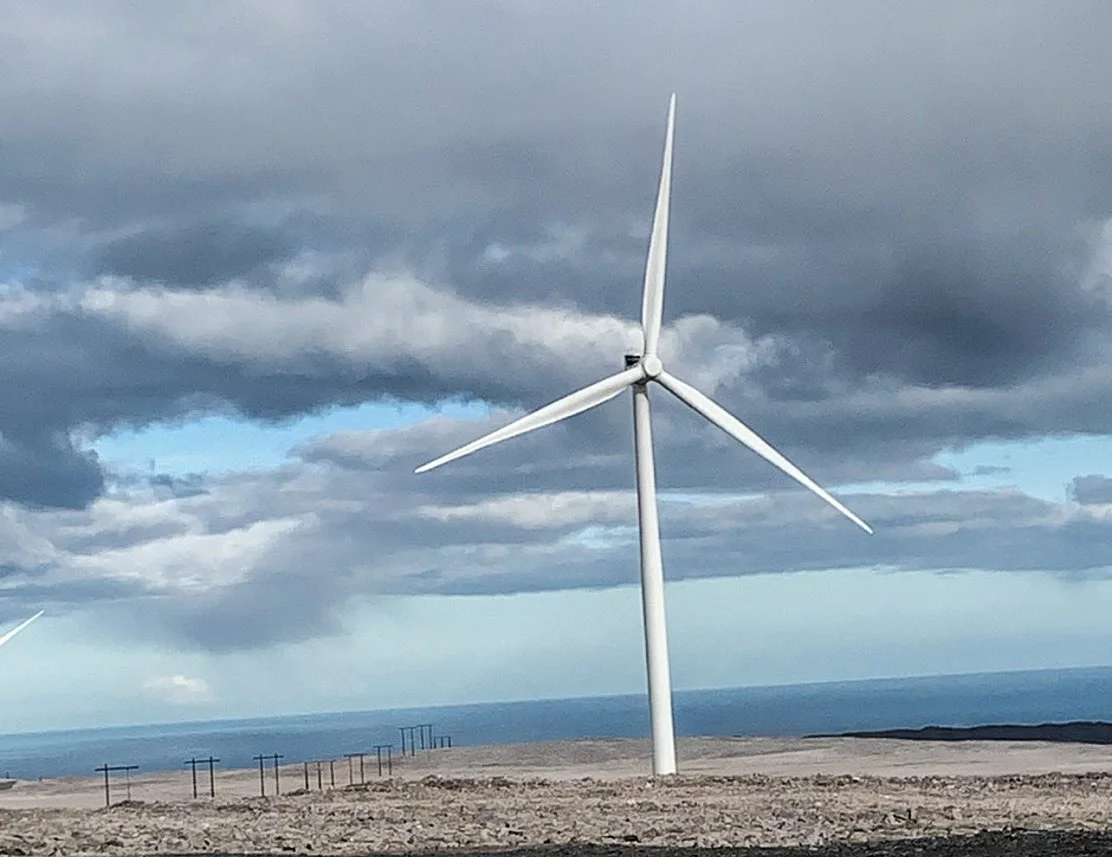 Vindturbin på Raggovidda med havet og mørke skyer i bakgrunnen.