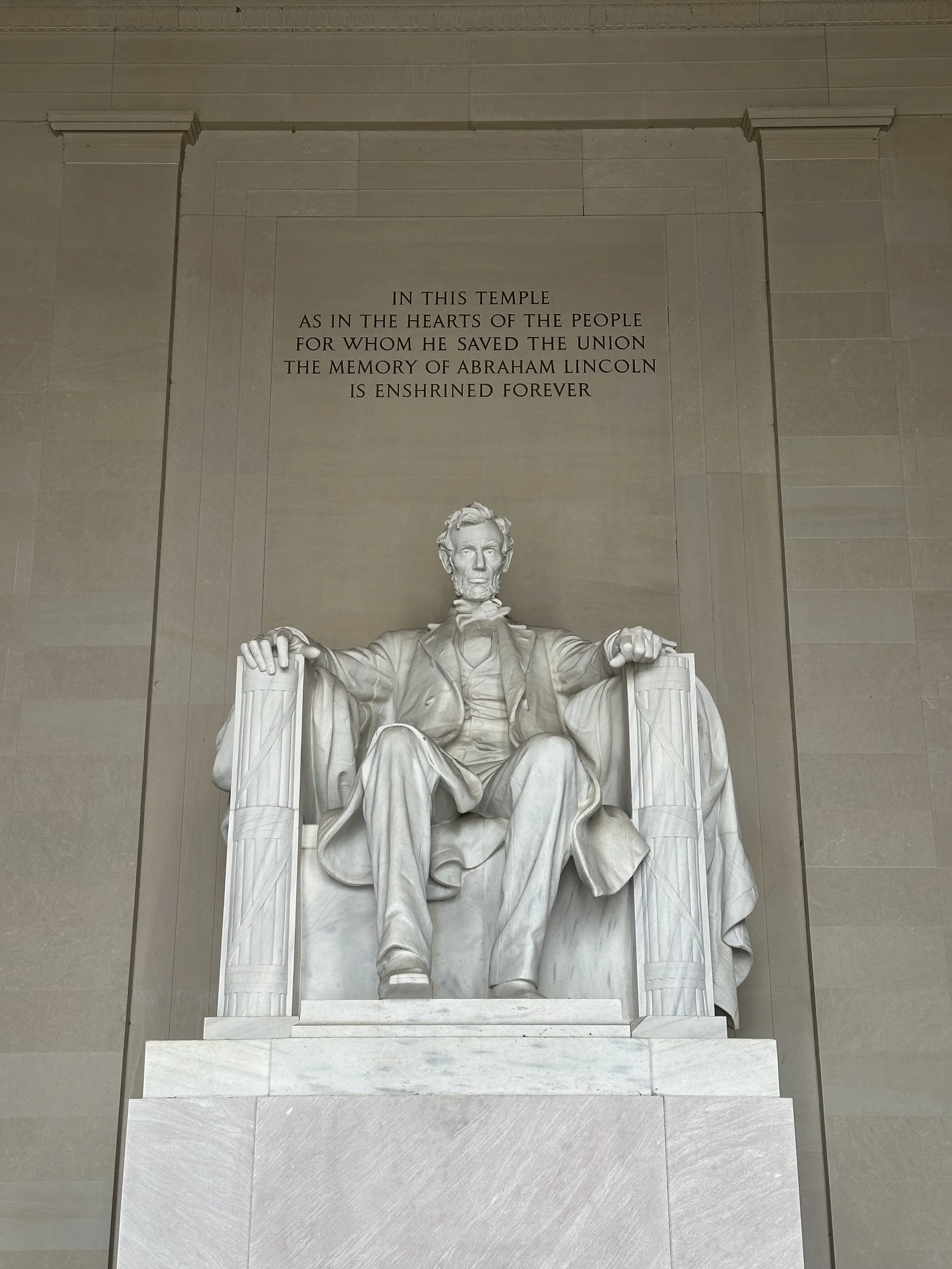 Den ikoniske marmorskulpturen av Abraham Lincoln sittende i Lincoln Memorial, med inskripsjonen på veggen bak og de monumentale søyleveggene som rammer monumentet inn.
