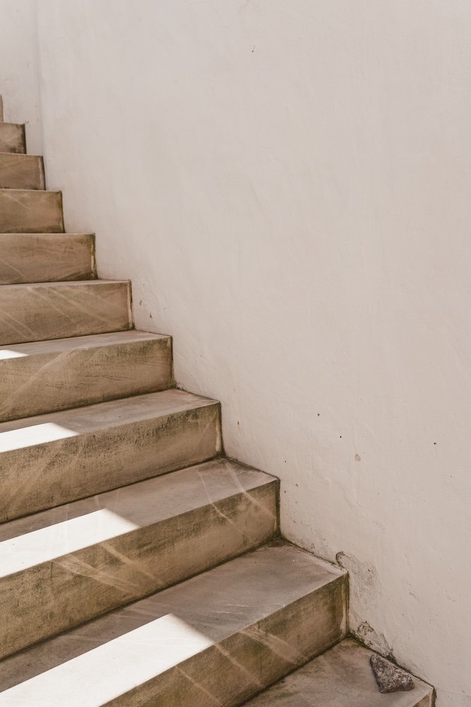 Indoor staircase with wooden steps and a white wall on the side, with sunlight casting shadows on the steps.