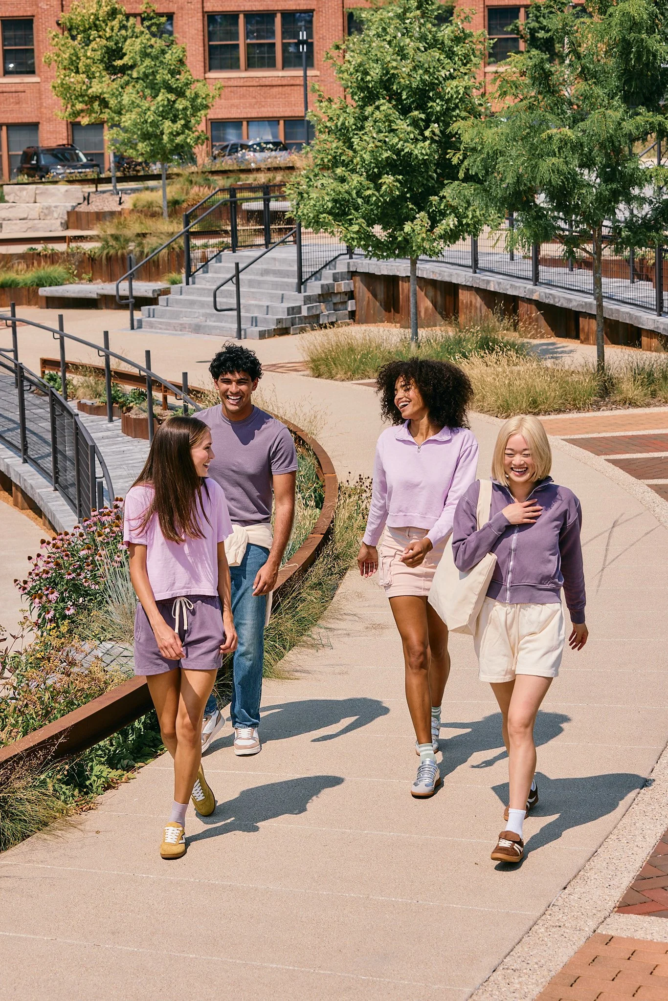 Four young women and one young man walking and laughing outdoors on a sunny day.