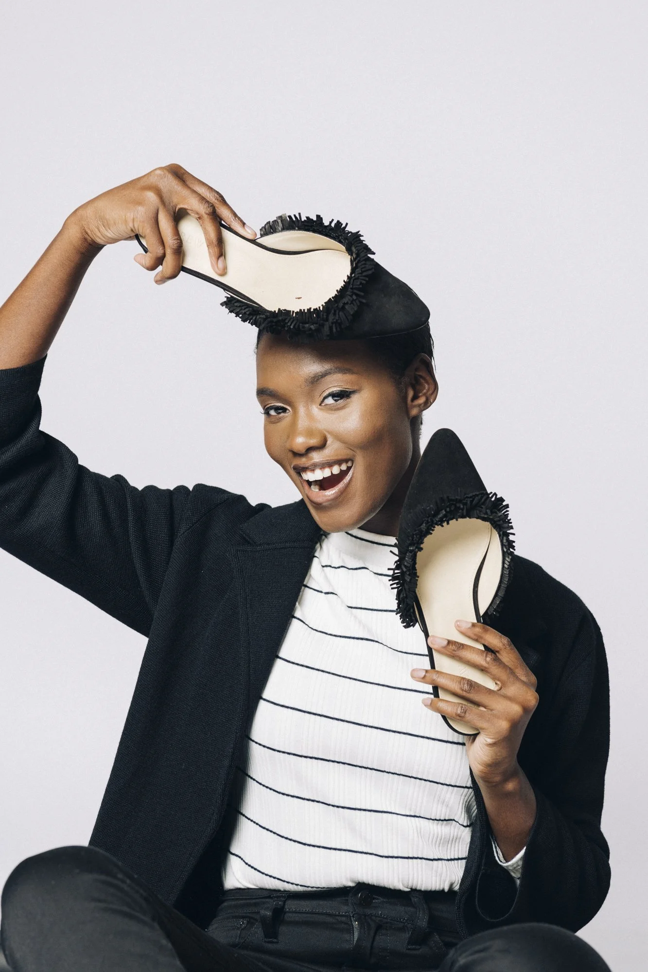 Woman smiling and holding two black and white shoes with fringes.