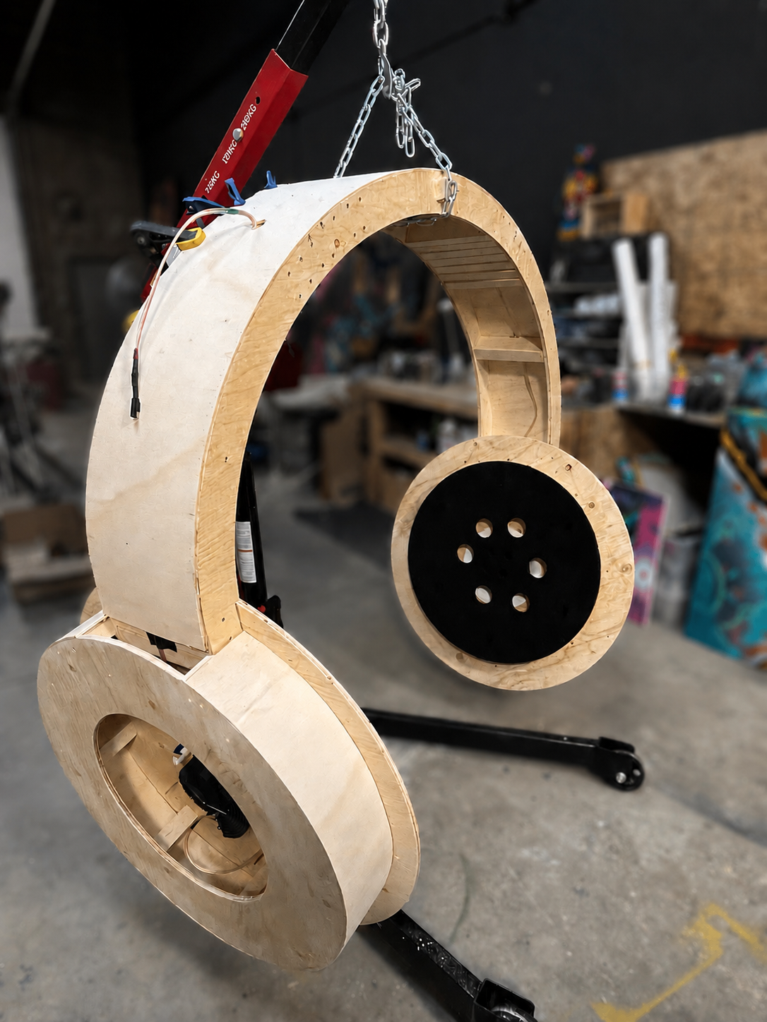 Un framework en forma de auriculares fabricado con madera y metal, con componentes electrónicos y cables, en un taller con herramientas y materiales en el fondo.