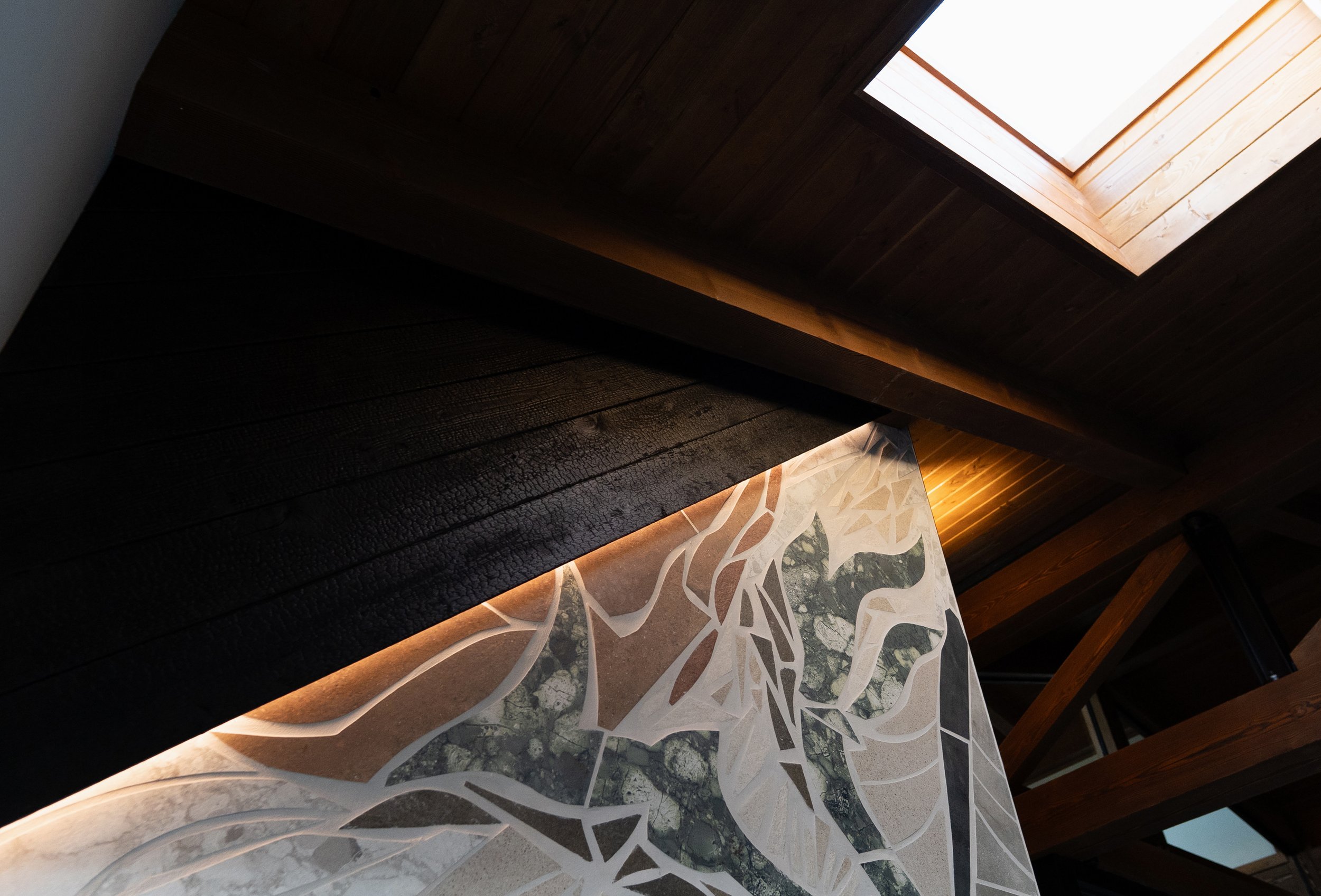 Interior view of a room with a wooden ceiling and a sky window. The trim of the window is made of wood, and the room has a patterned floor with shades of gray, white, and black.
