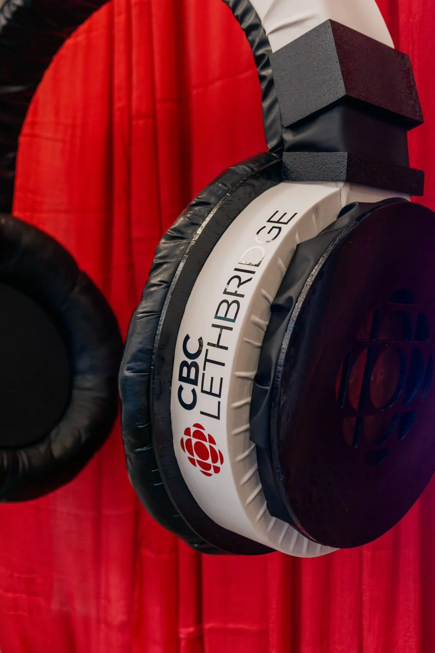 Close-up of a set of headphones with the CBC logo and the words CBC LETTHBRIDGE, placed on a red curtain background.