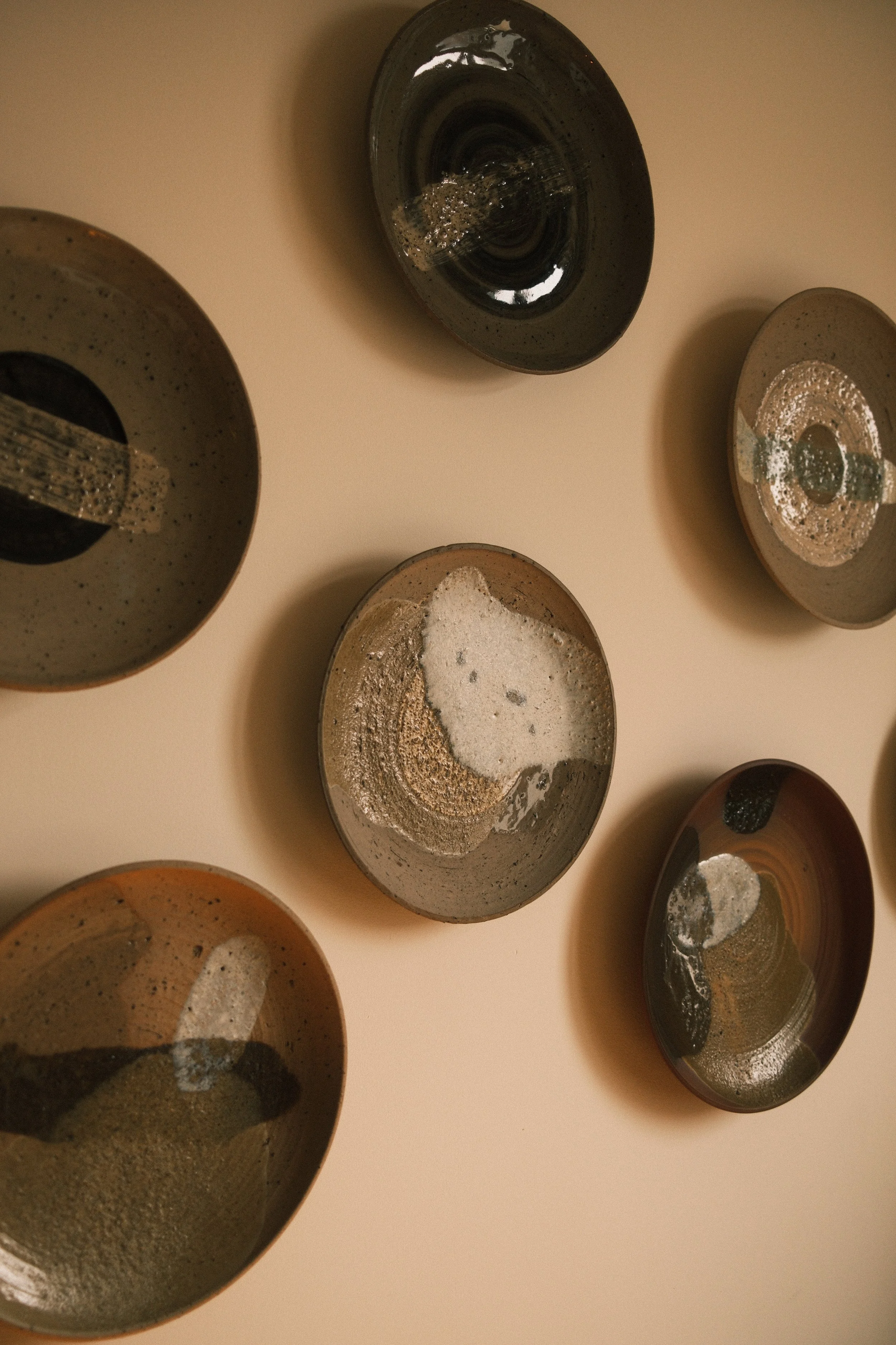 Multiple ceramic bowls with various glazing patterns and textures, some containing foam or residue, placed on a beige surface.