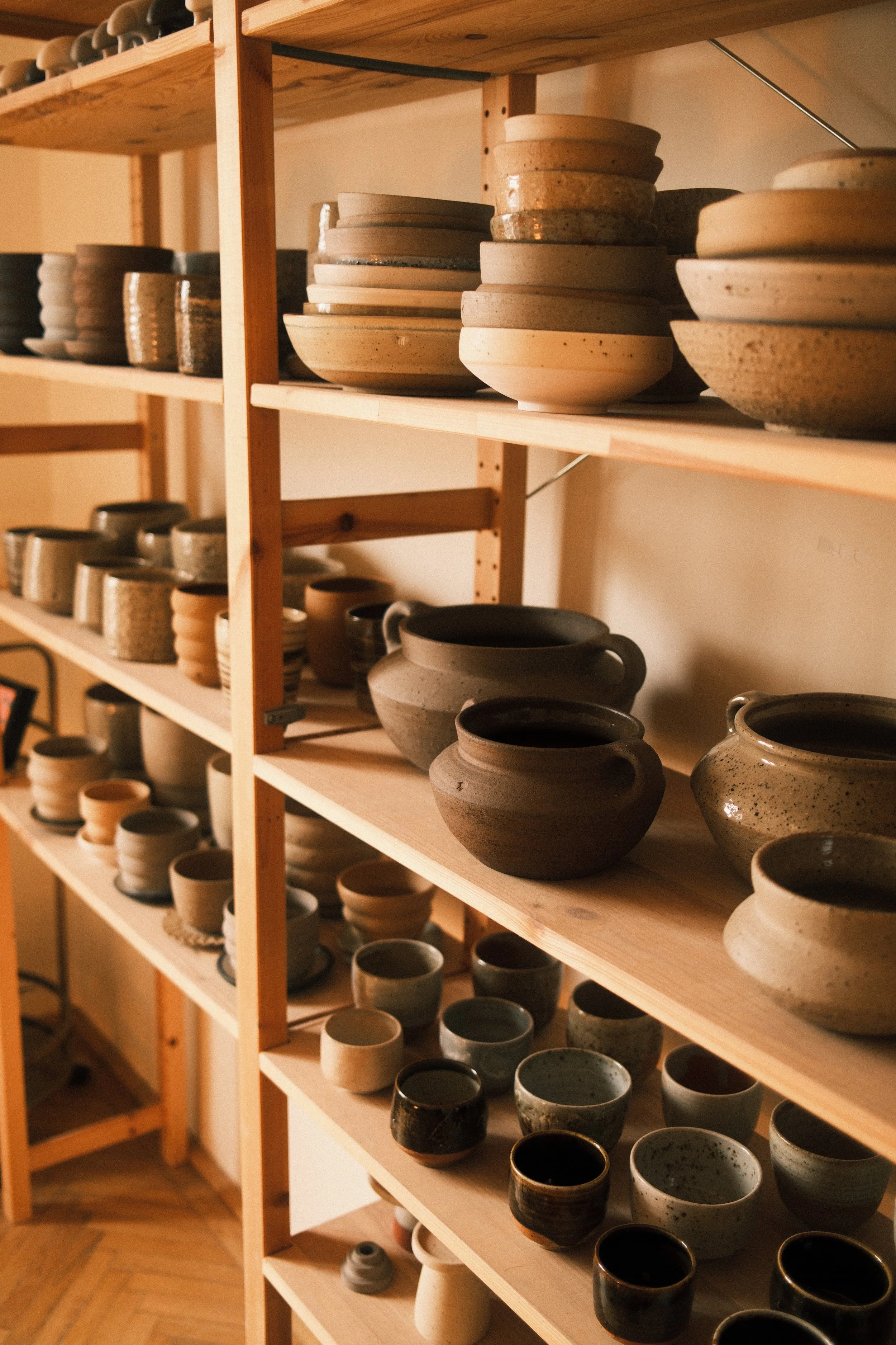 A wooden shelf filled with various handmade ceramic bowls and mugs in different colors and textures.