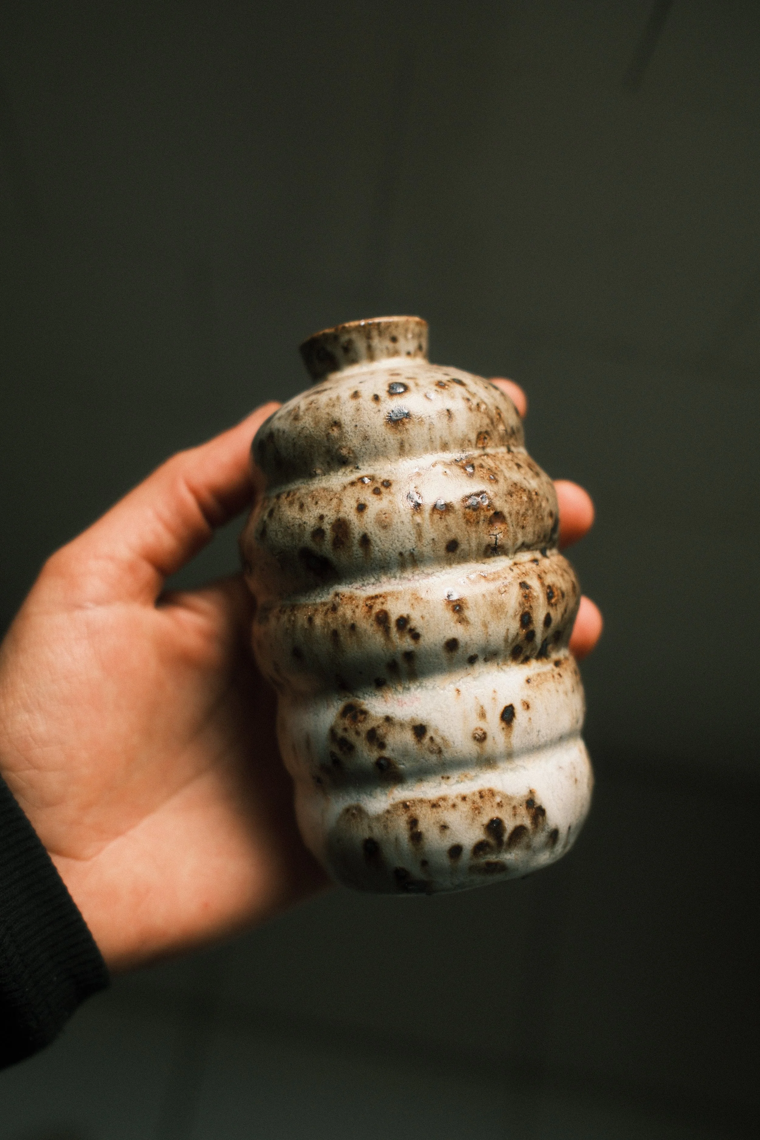 Close-up of a hand holding a beige and brown ceramic sculpture with a spiral, layered design.