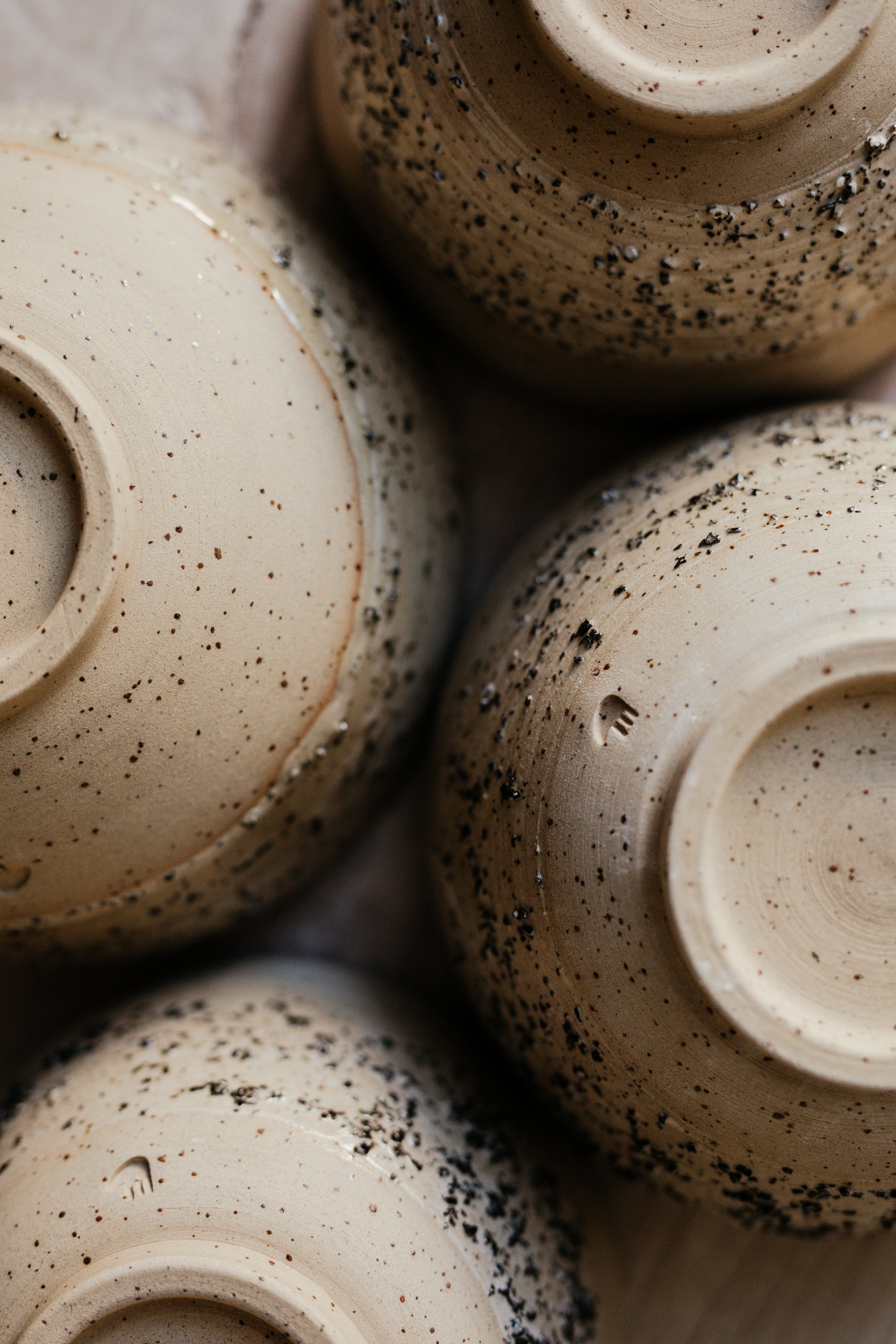 Close-up view of the bottom of beige ceramic cups with speckled black and brown patterns.
